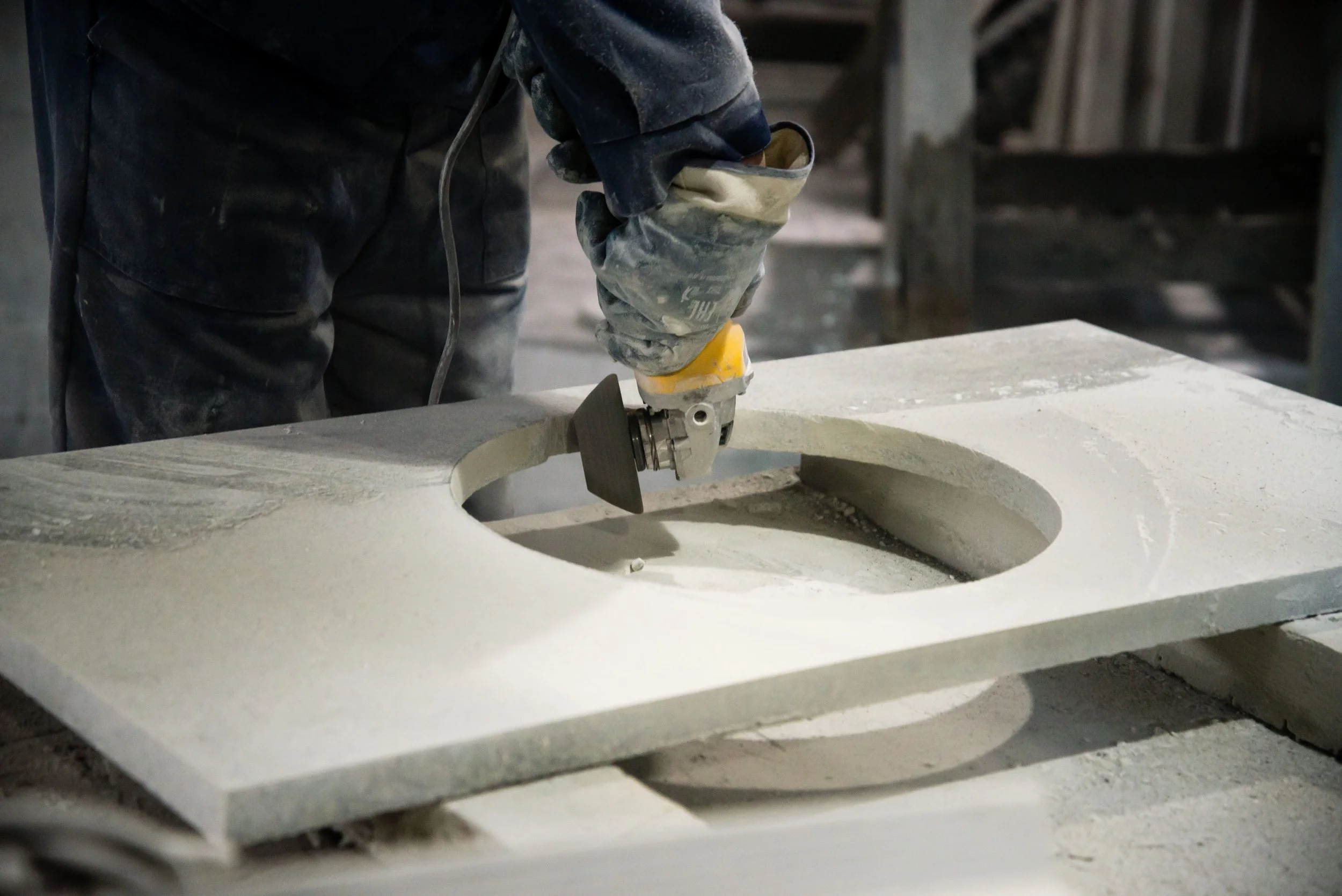 A worker shaping a large piece of stone using a power grinder in a workshop.