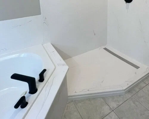 Bathroom featuring a bathtub with black fixtures and a separate shower area with a gray drain on the floor.