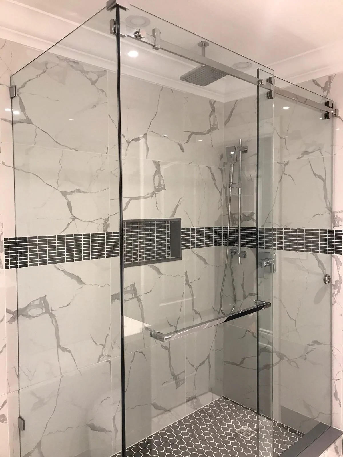 Marble Tradition, bathroom renovation in Kitchener-Waterloo & Cambridge, Ontario. Modern glass-enclosed shower with marble walls, a built-in niche, and hexagonal tile flooring.