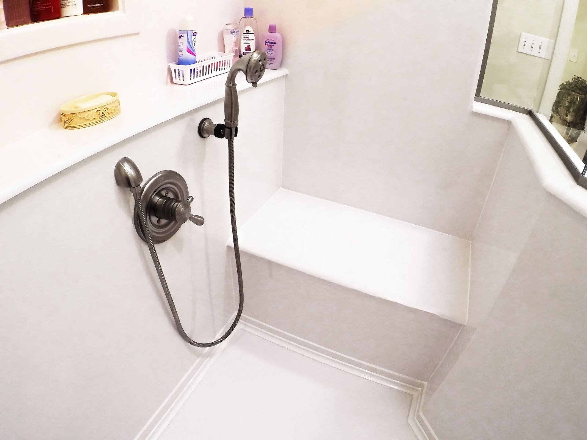 Marble Tradition, bathroom renovation in Kitchener-Waterloo & Cambridge, Ontario. A hospital or assisted living shower with a handheld showerhead and a built-in bench, surrounded by white walls and a small window.