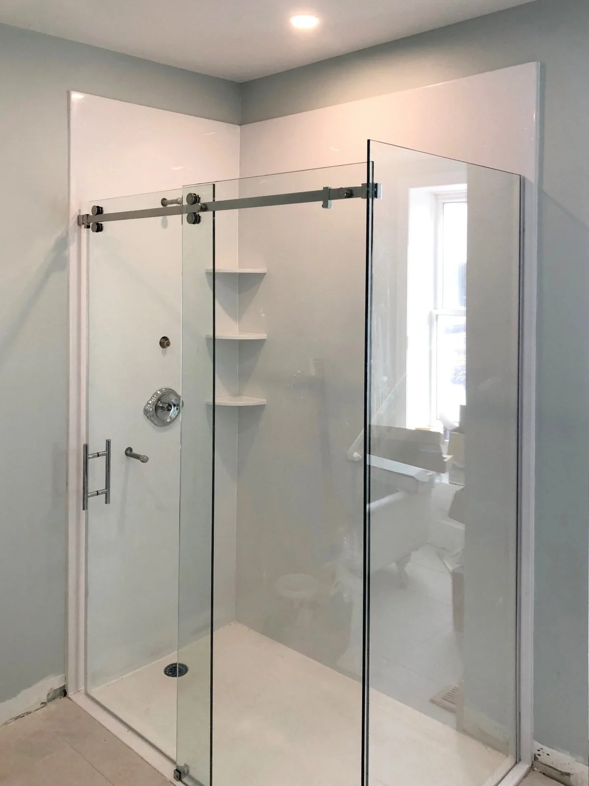 A modern bathroom shower with glass walls, built-in shelves, a window, and a rain showerhead.