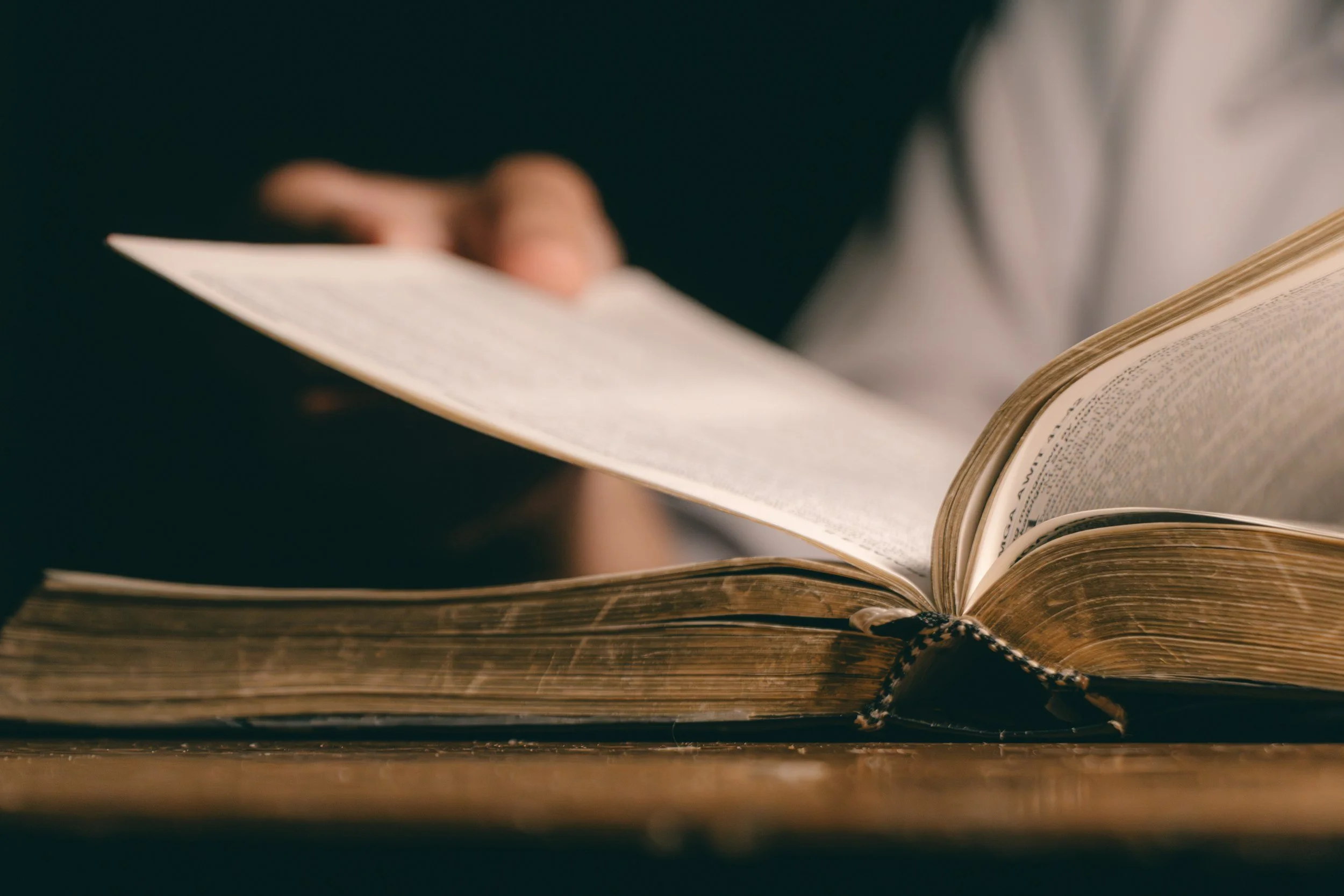 Close-up of a person holding an open book with worn pages on a wooden surface.