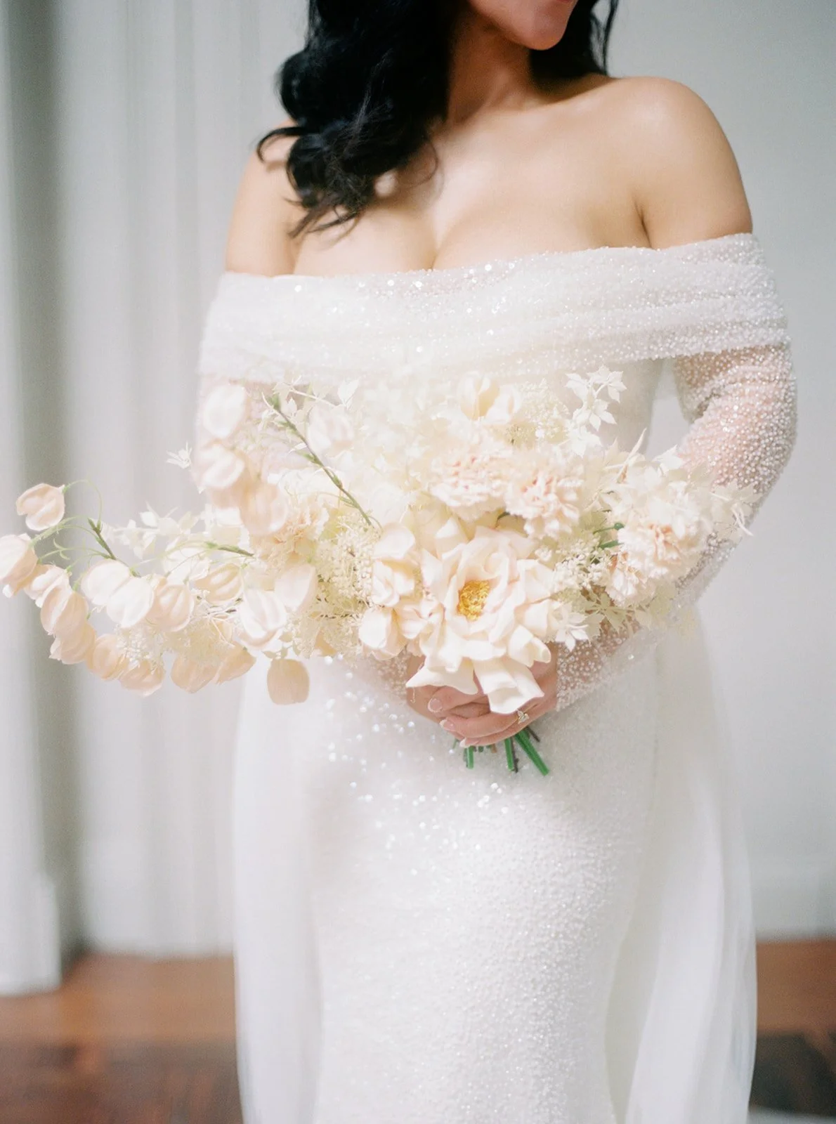 A woman in an off-shoulder white dress holds a bouquet of pink and cream flowers.