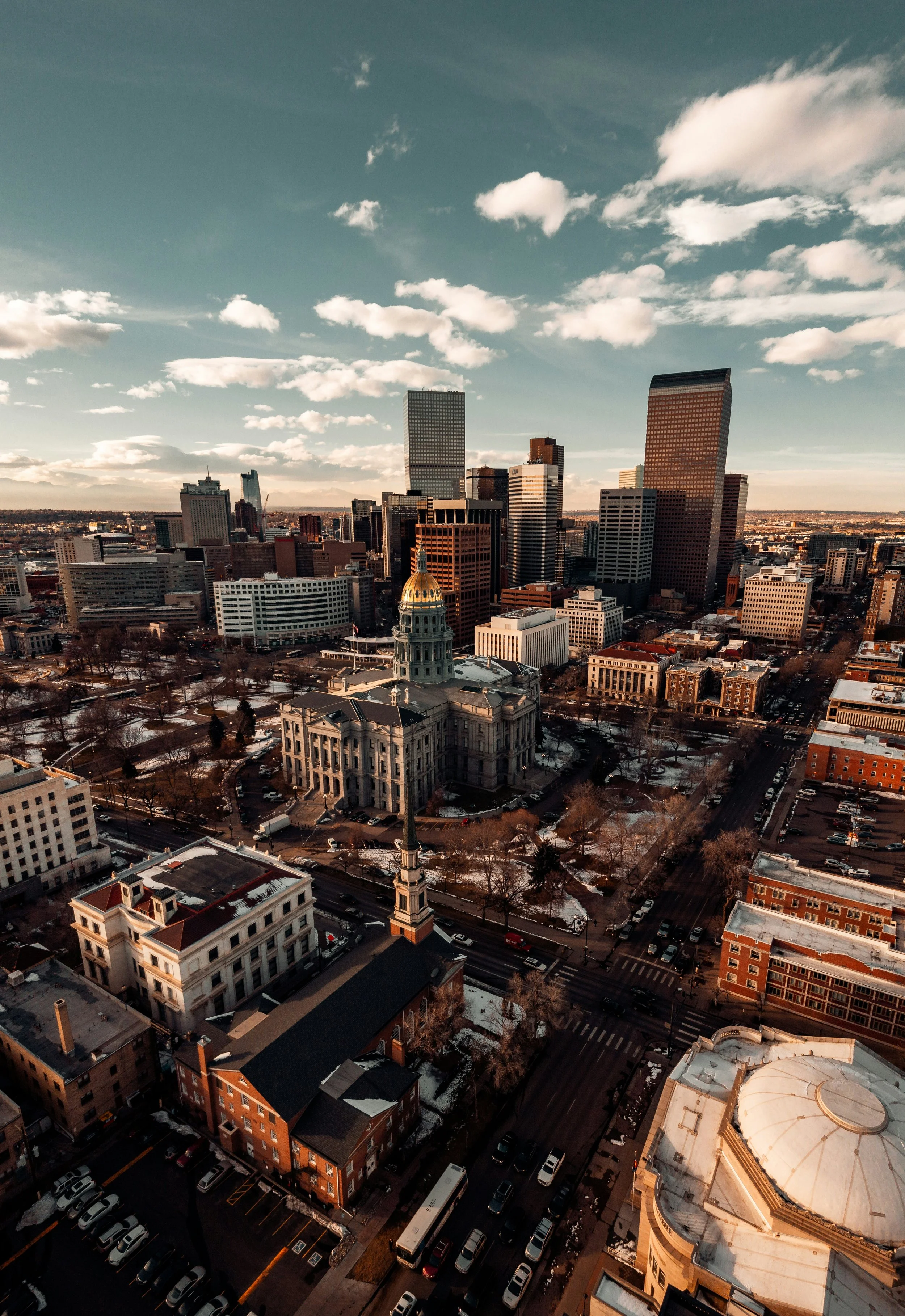 A cityscape with tall buildings, including a dome-topped structure with a clock, under a partly cloudy sky during sunset.