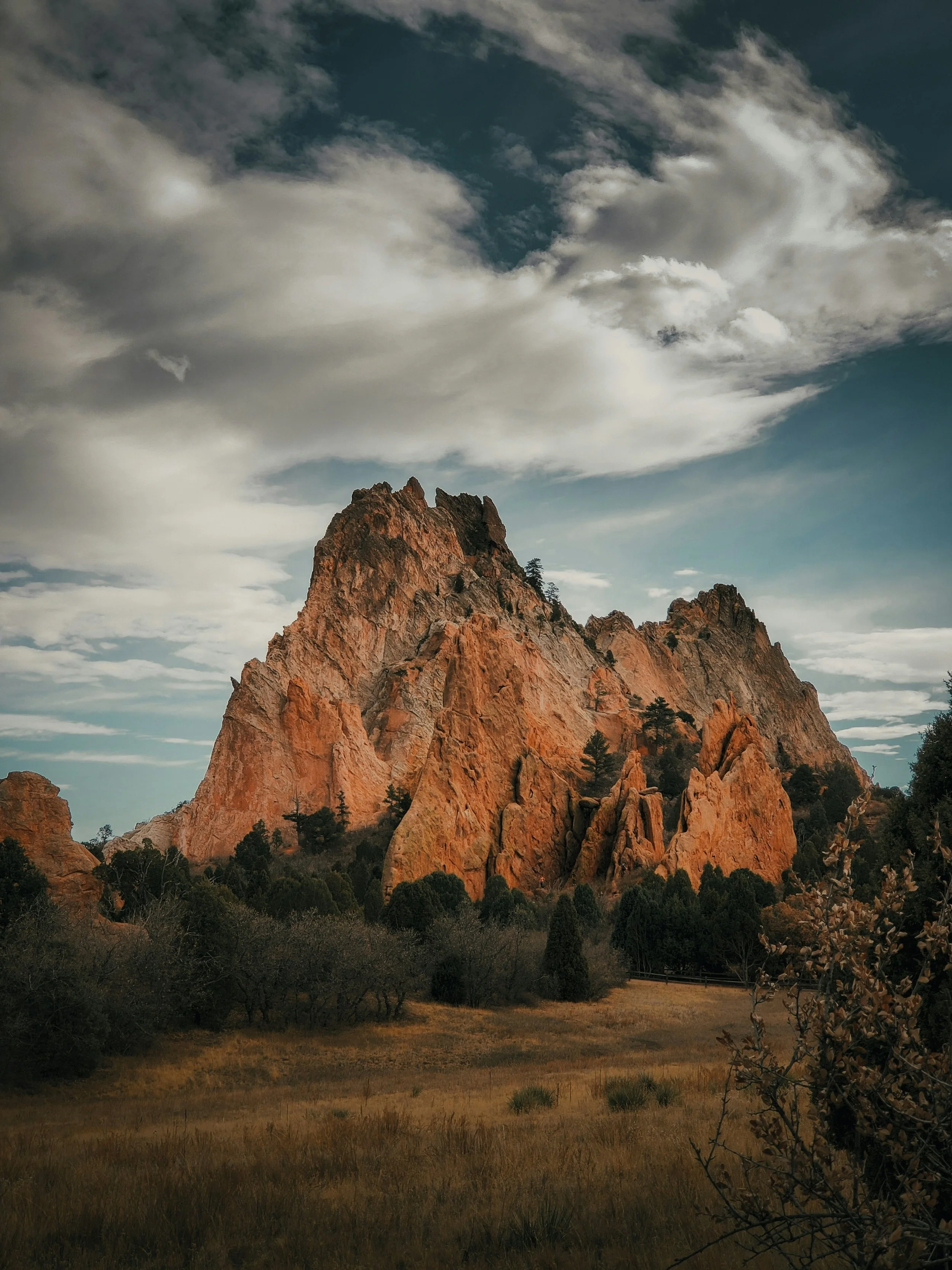 A rocky mountain with trees at its base under a sky with scattered clouds.