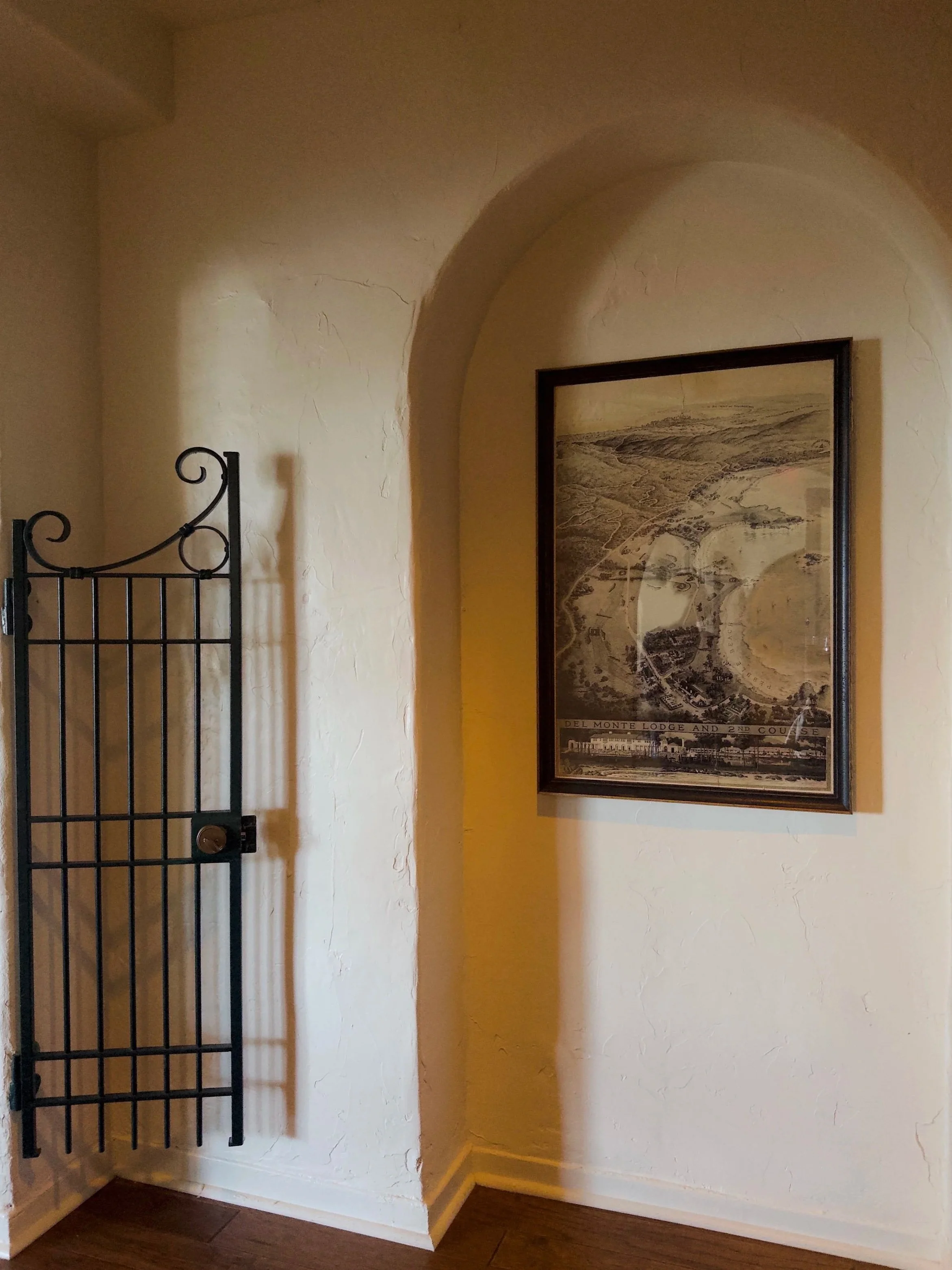 Interior wall with textured white stucco, a framed vintage map or city plan, and part of a black decorative metal gate or railing.