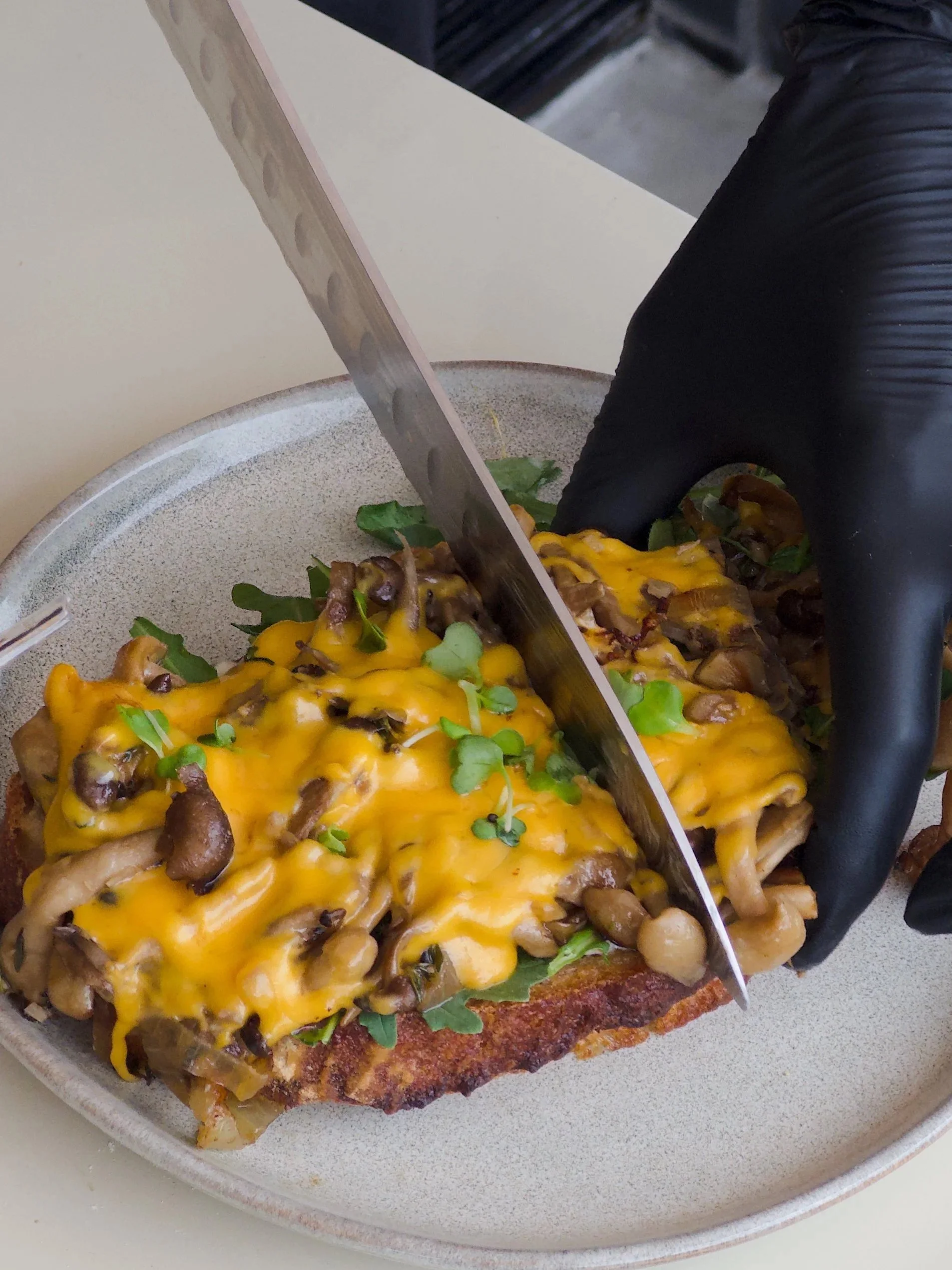 A slice of loaded cheesy french fry topped with melted cheese, mushrooms, and greens, being cut with a knife.