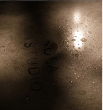 Close-up of a wet surface with the words 'SOA STUDIOS' reflected on it and water droplets, illuminated by a bright light.