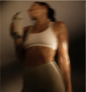 A woman in a white sports bra and gray leggings holding a phone, with motion blur.