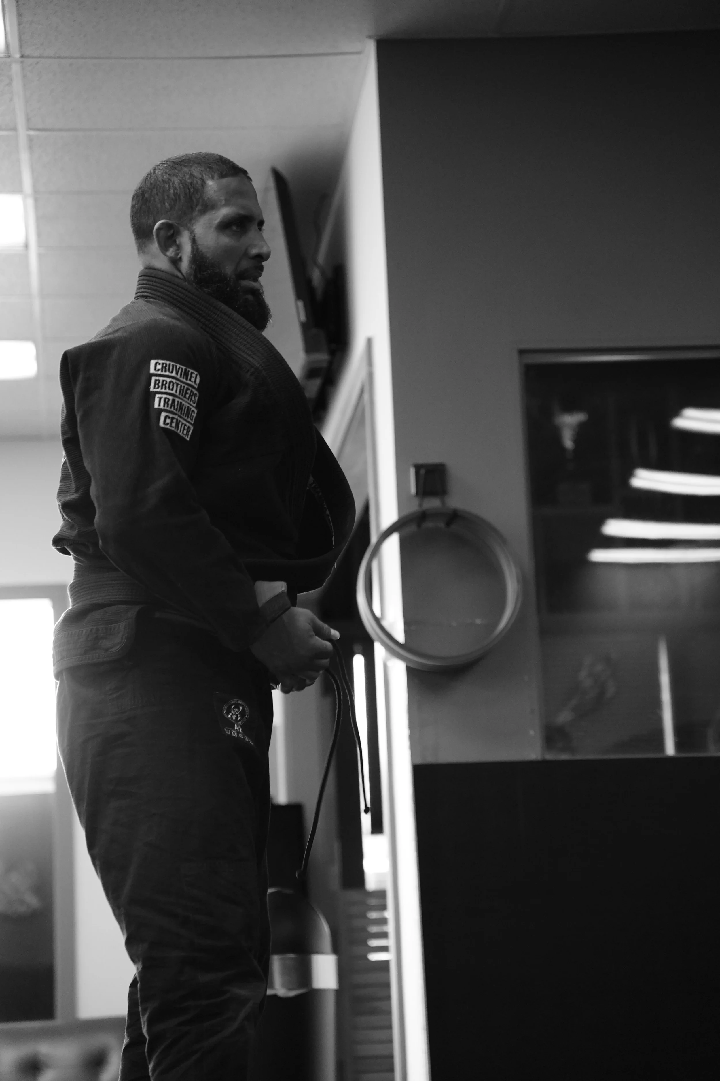 A man wearing a martial arts uniform sitting and looking to the side in an indoor training facility.