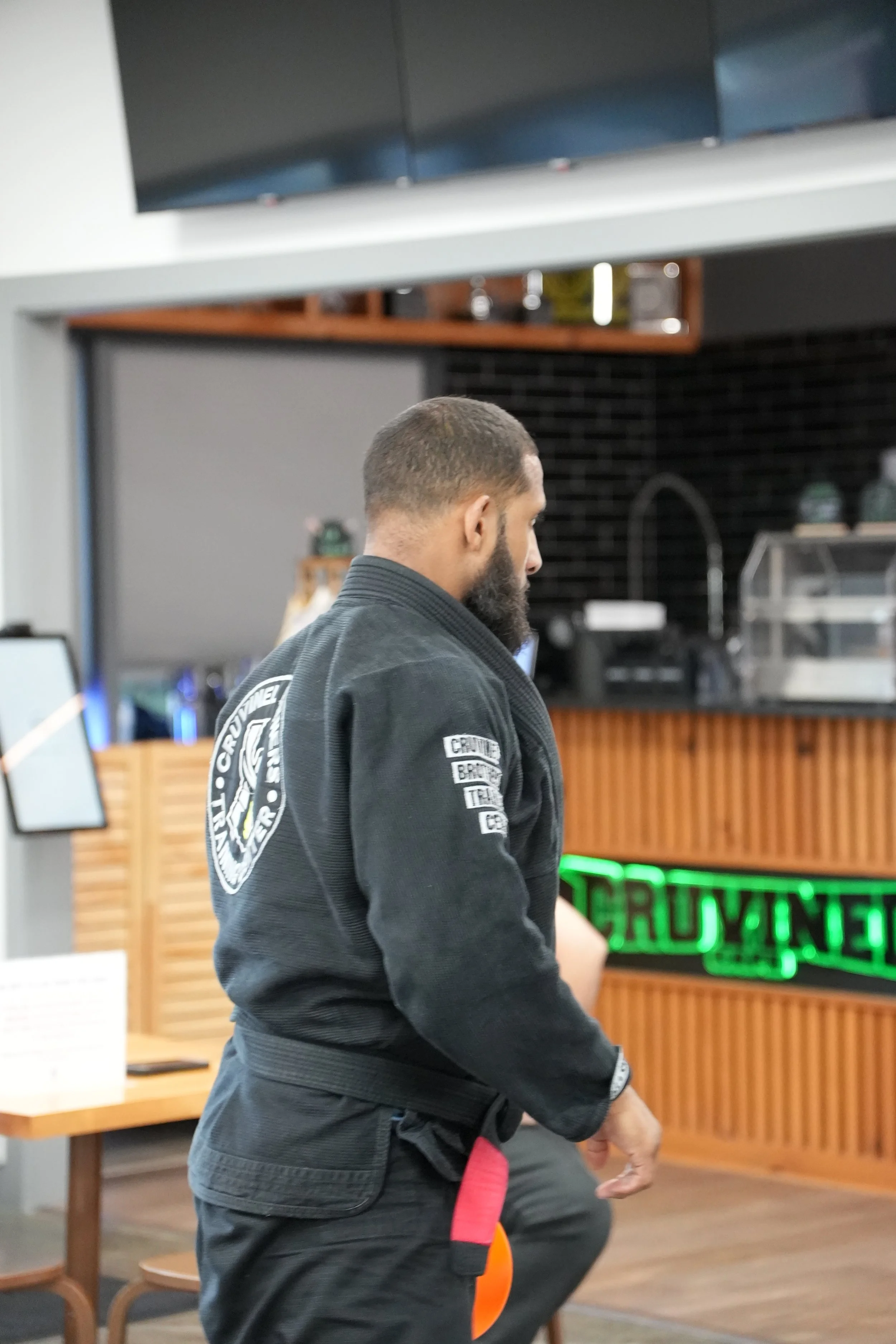 Man in martial arts gi with a red belt, practicing martial arts in a restaurant or café.