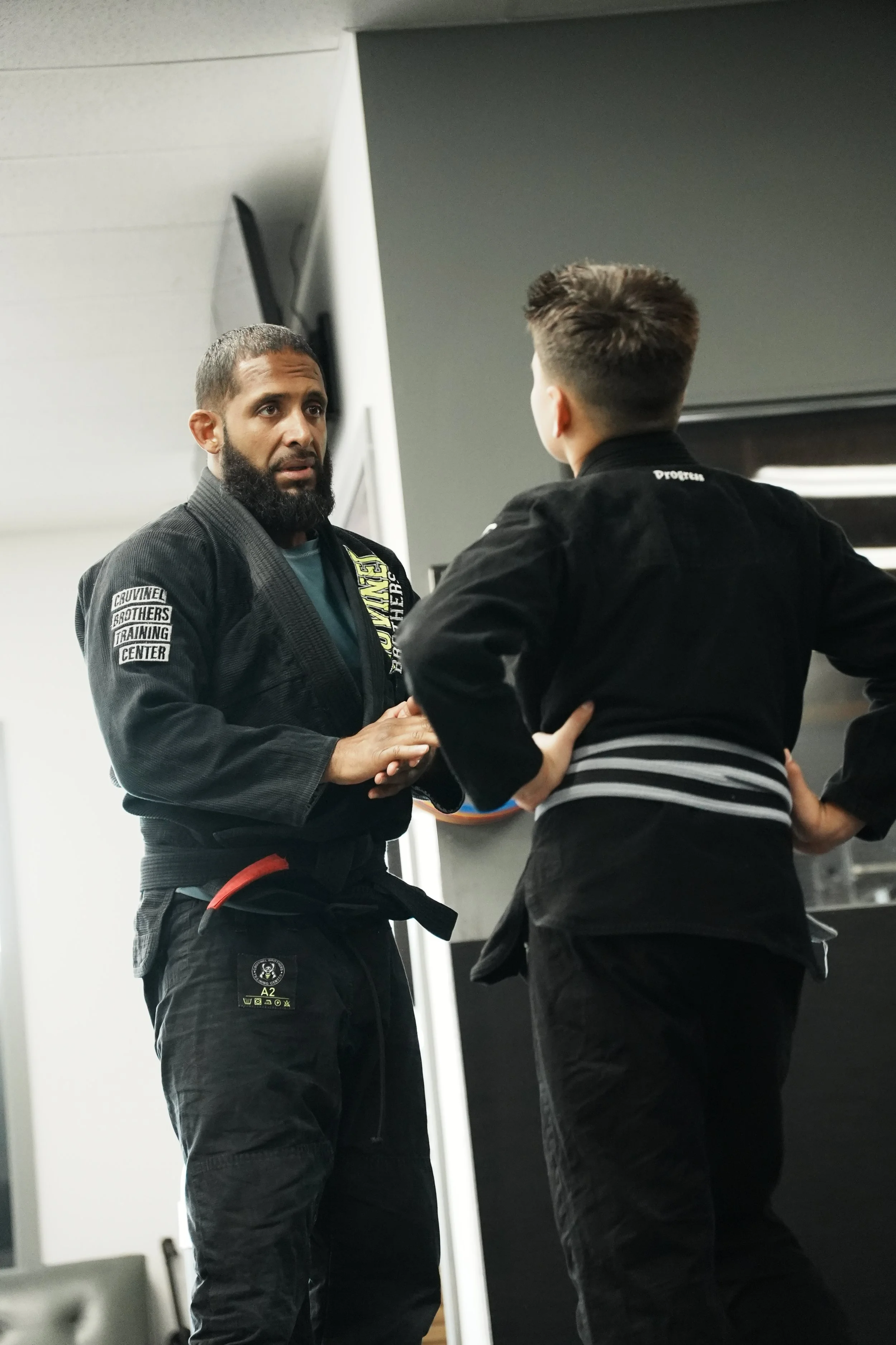 Two martial artists in black uniforms having a conversation in a martial arts training facility.