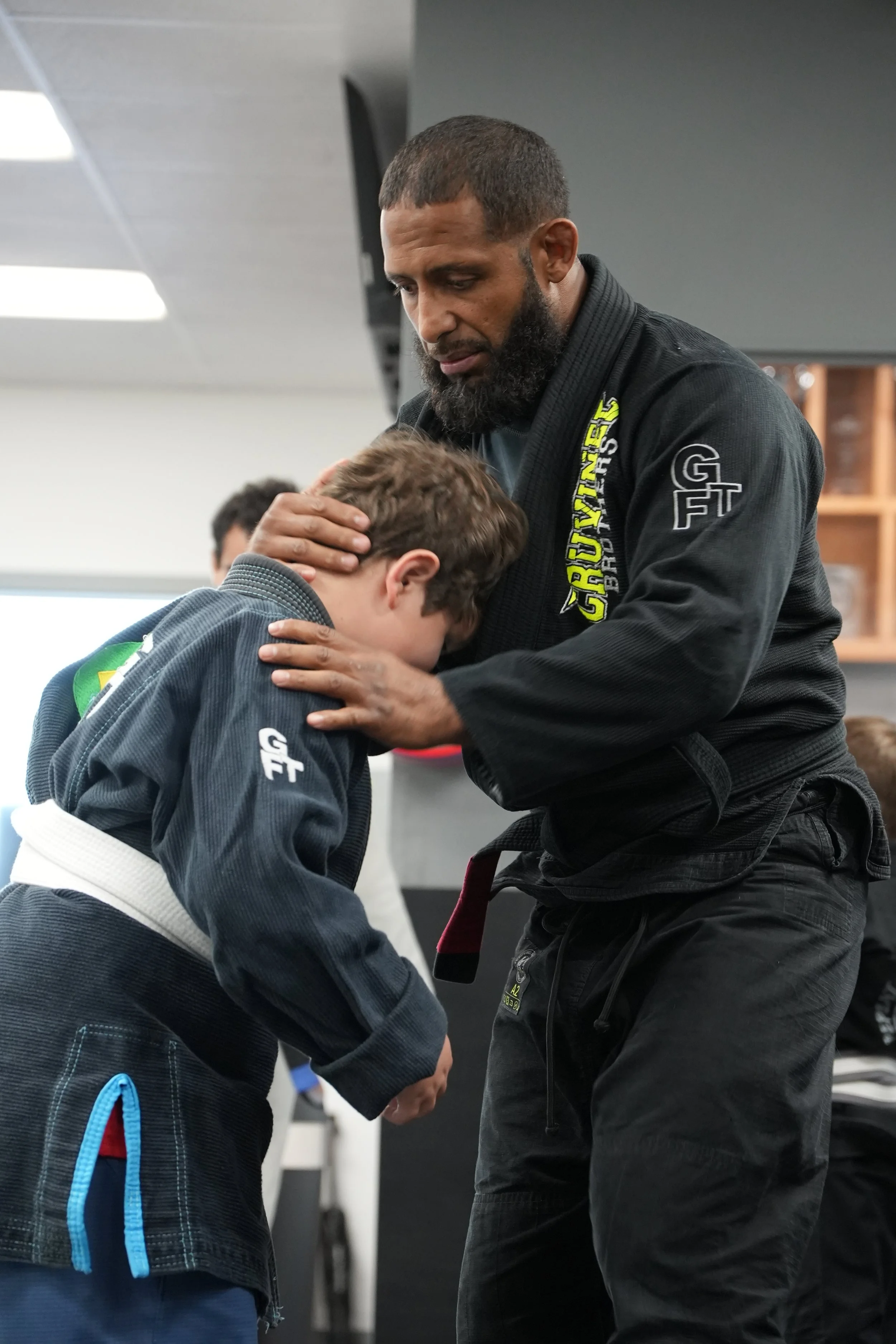 An instructor demonstrating a Brazilian Jiu-Jitsu technique with a young student in a martial arts training facility.