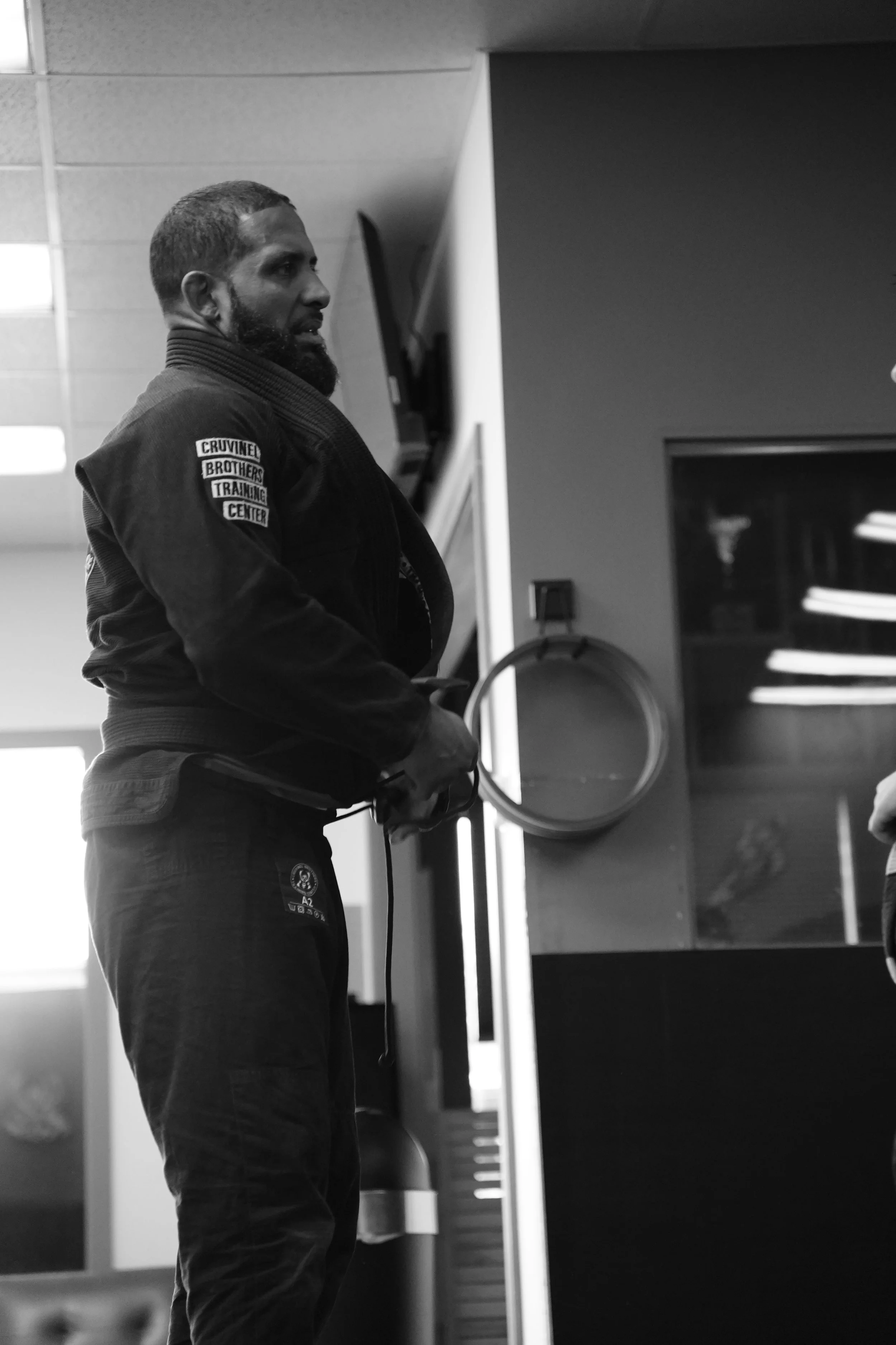 A man wearing a martial arts gi with a patch that says 'Cruvinel Brothers Training Center' stands in a gym or training facility, holding a jump rope.