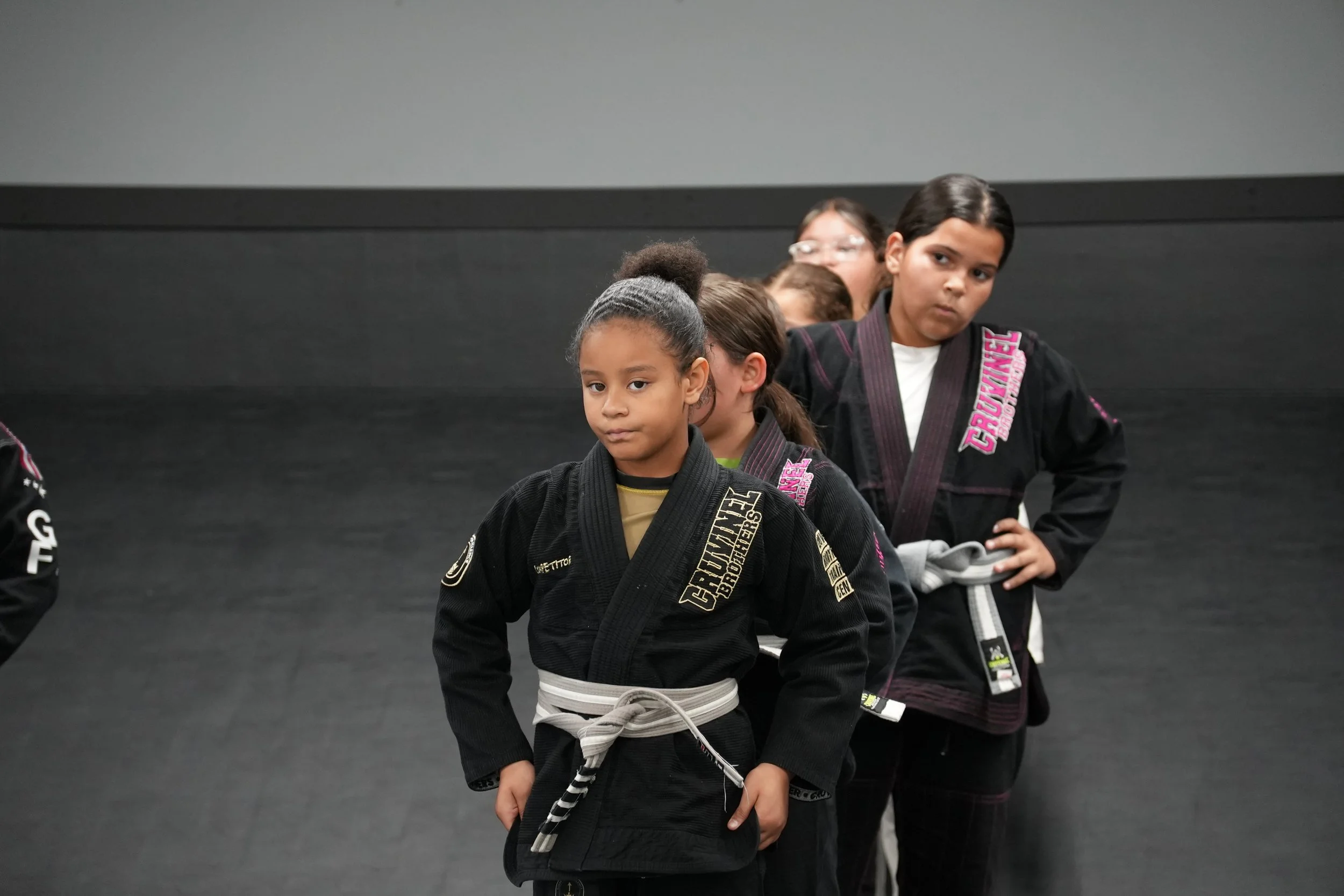 Group of children in martial arts uniforms standing in a line indoors.
