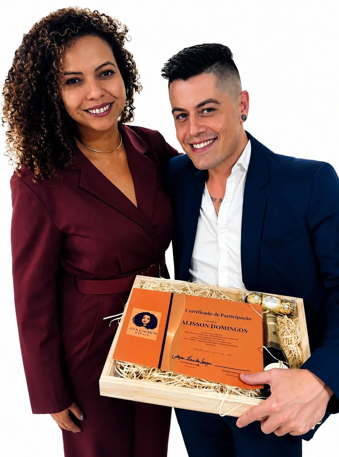 Homem e mulher sorrindo, segurando uma caixa de presente com certificado de participação, uma garrafa de espumante e bombons, em fundo branco.