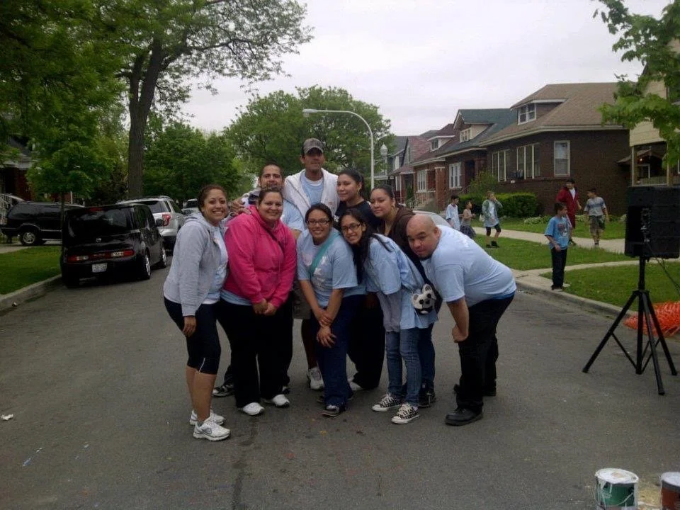 Group of people standing together outside on a residential street, smiling and posing for a photo.