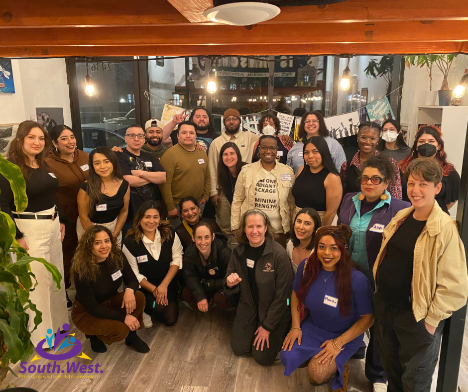 A diverse group of people, mostly women, gathered in a restaurant or cafe for a photo, with some wearing masks and name tags, smiling and posing for the picture.