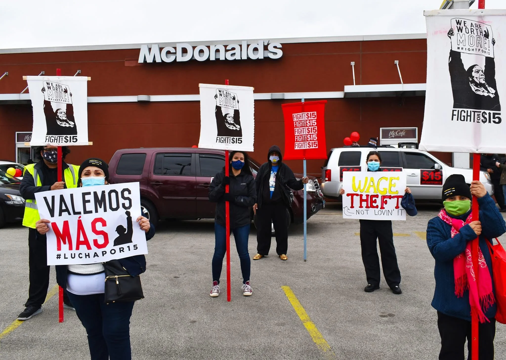 A group of people protesting outside a McDonald's, holding signs with messages about workers' rights and wages, in front of a McDonald's restaurant.