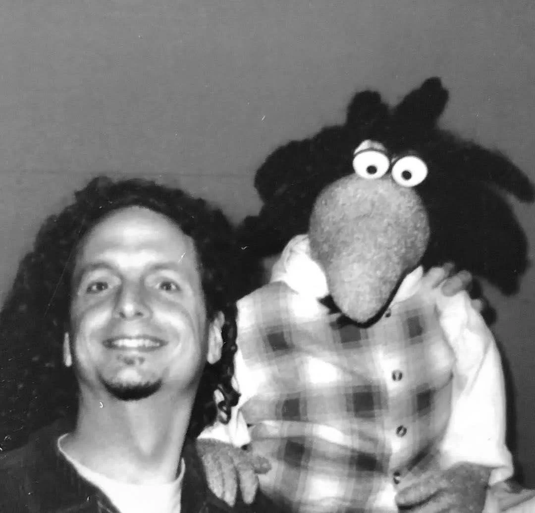 Black and white photo of a beaming Richard Gibbs with dark curly hair, and the muppet named after him.