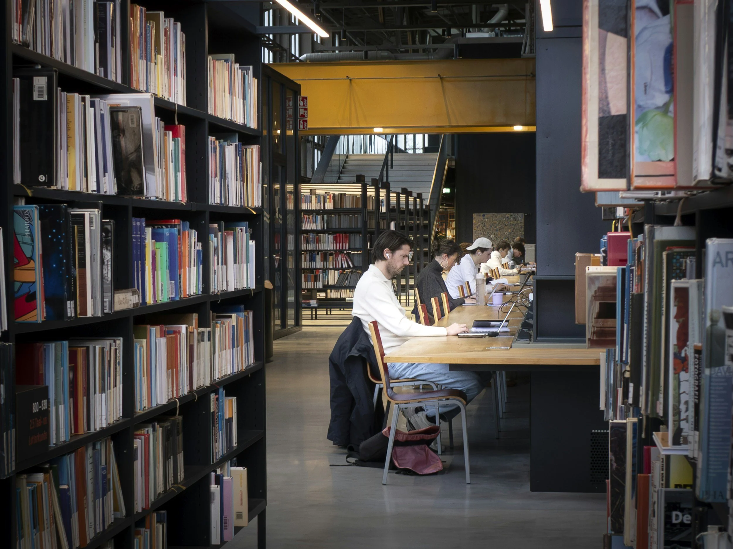 People working at a long table in a library with bookshelves in the background.