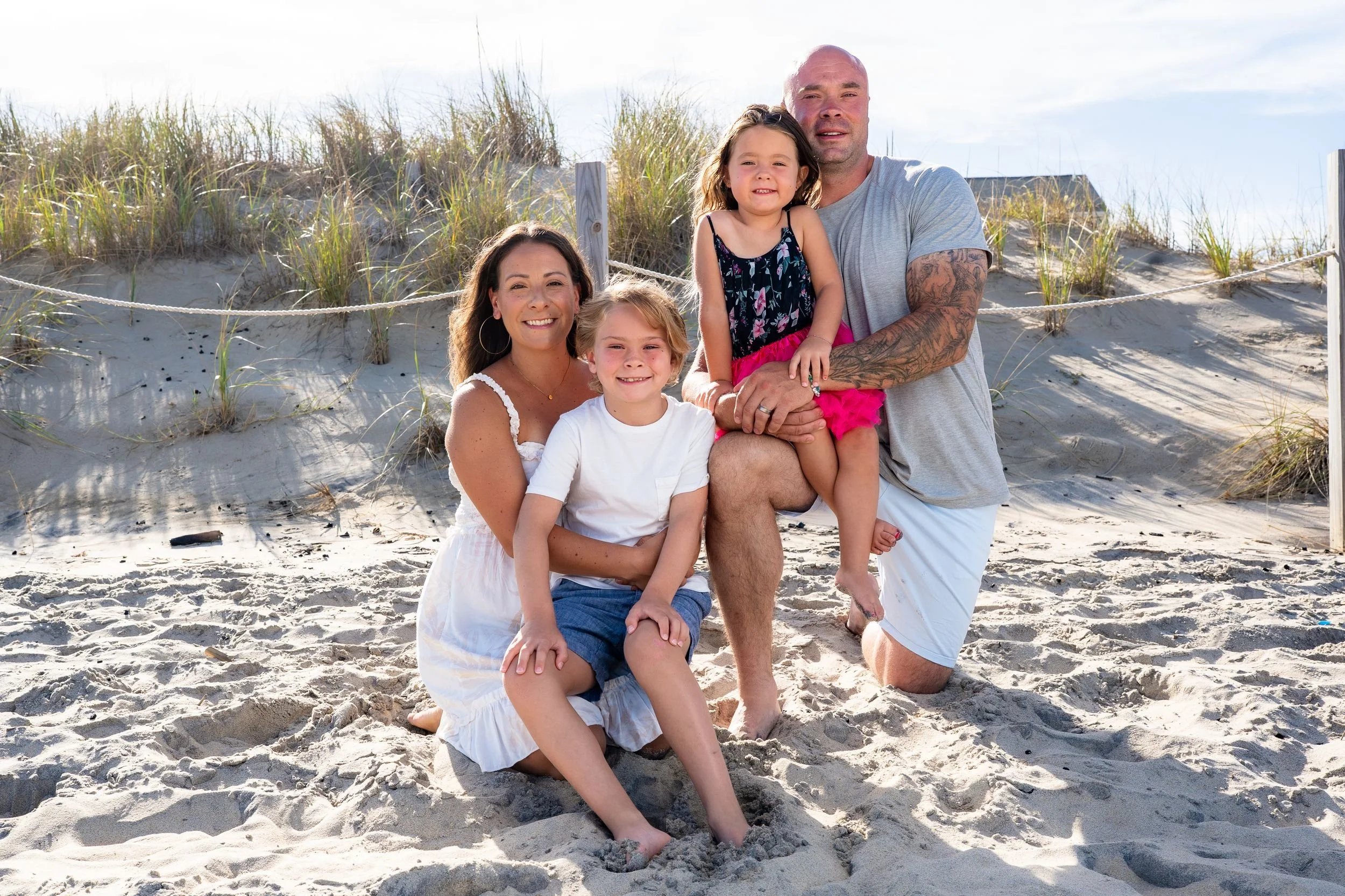 Family of five smiles during a beach family portrait session with sand dunes and beach grass in the background.