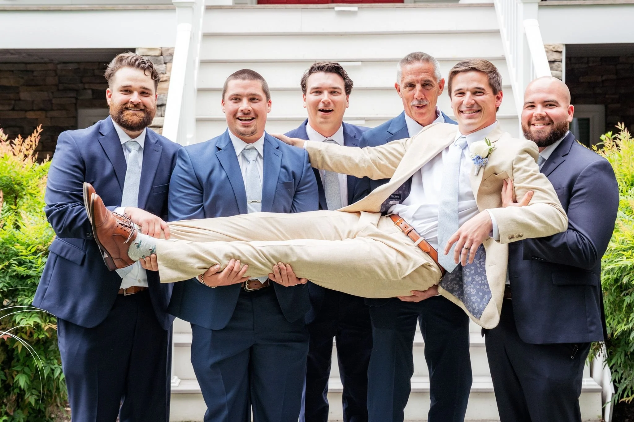 Groomsmen lift groom during fun wedding party portraits before a Maryland wedding reception.