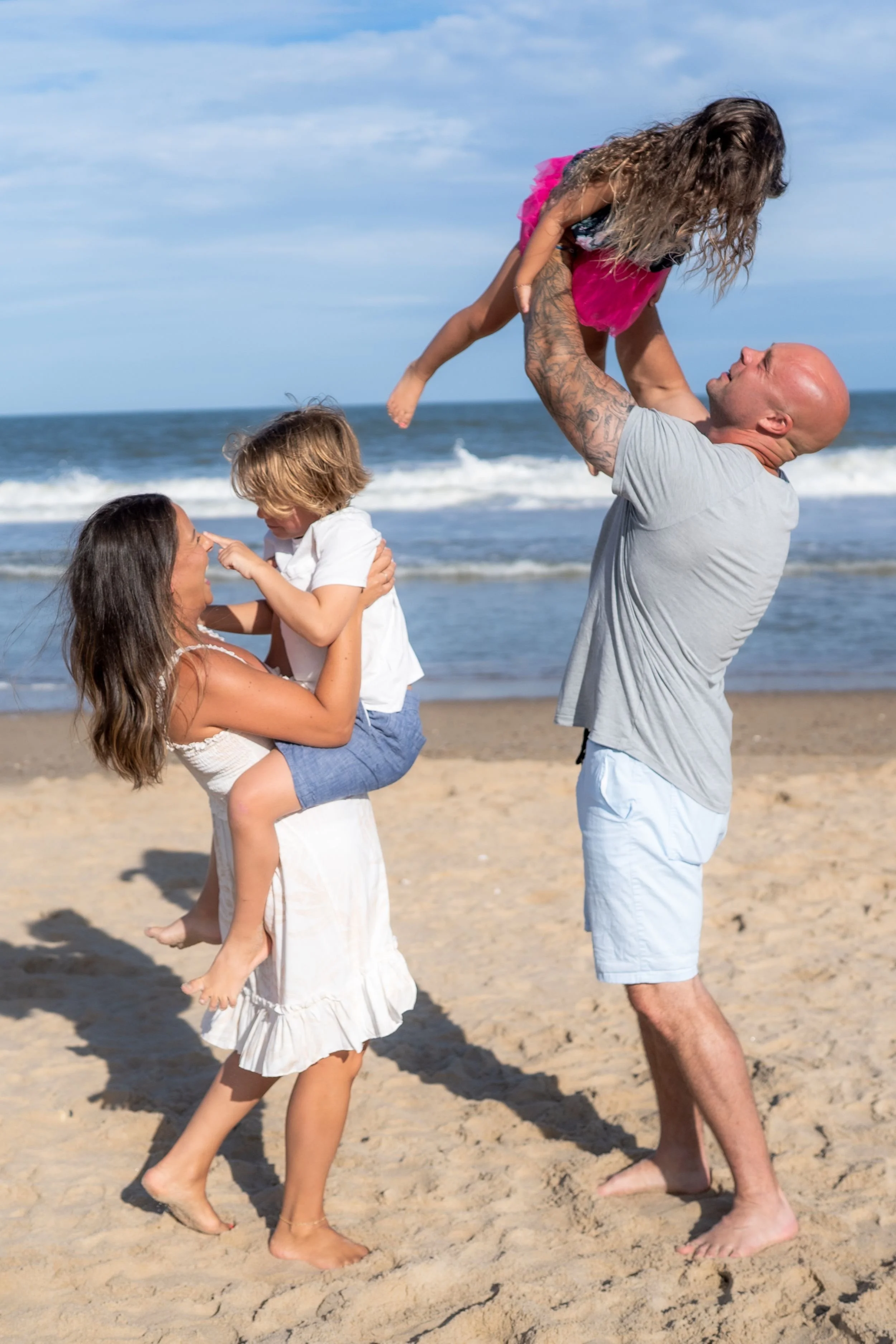 Family of four enjoying a relaxed beach portrait session on the Eastern Shore, with parents playing with their young children near the ocean.