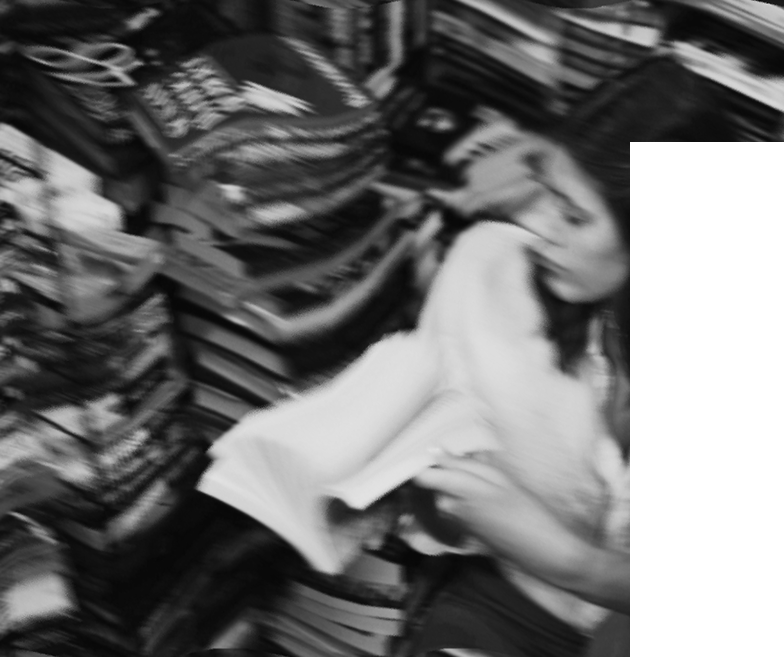 A woman with long hair shopping in a bookstore aisle with shelves filled with books.