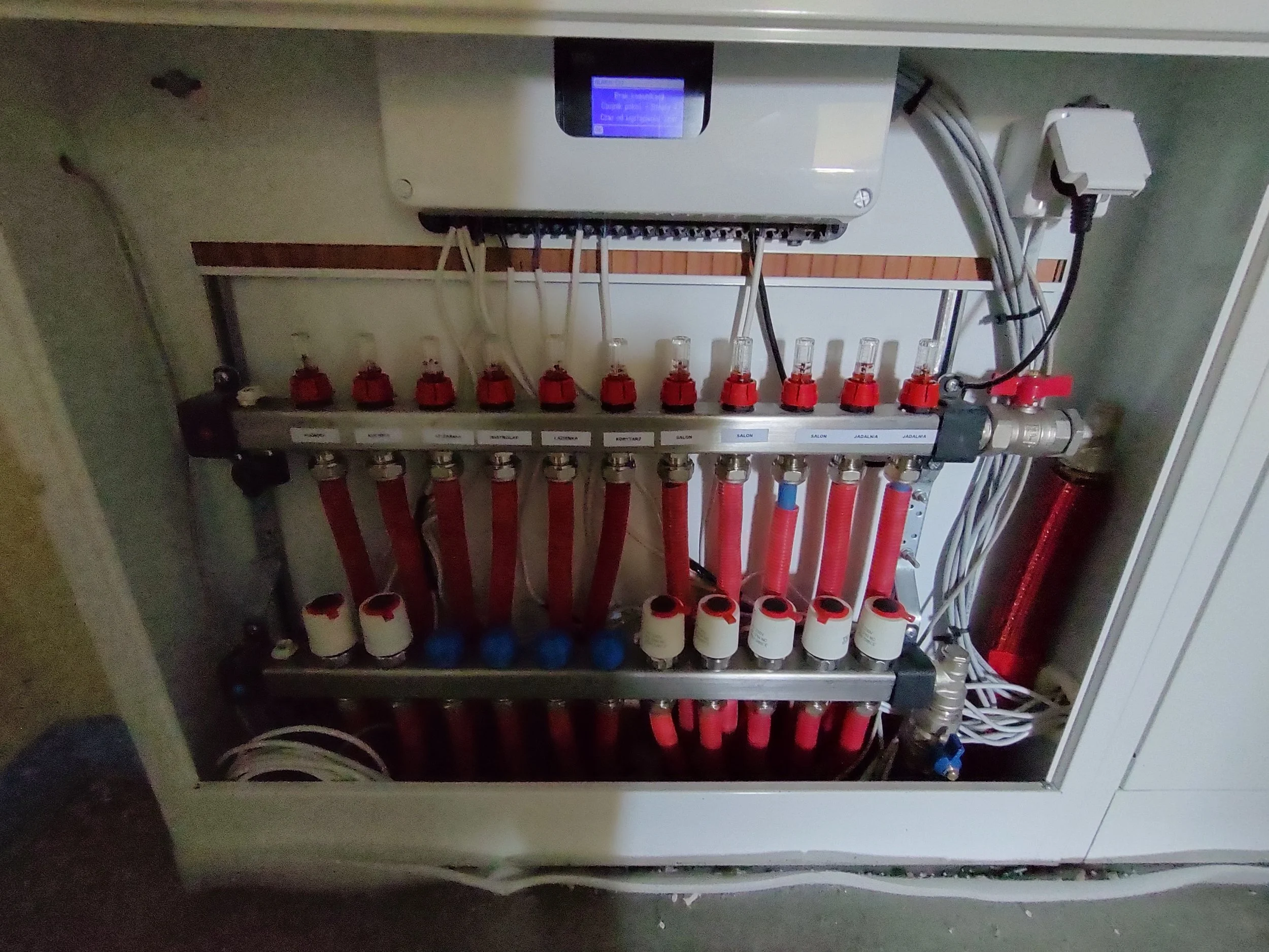 A grey electrical panel with multiple circuits and red and blue pipes connected to it, mounted inside an enclosure.