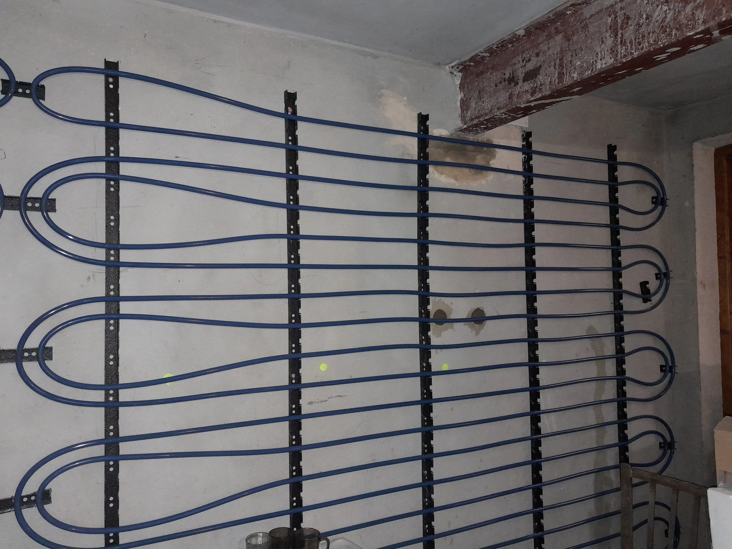 A construction site interior with a metal frame wall, blue electrical wiring, and a partially plastered wall showing exposed brick and insulation.