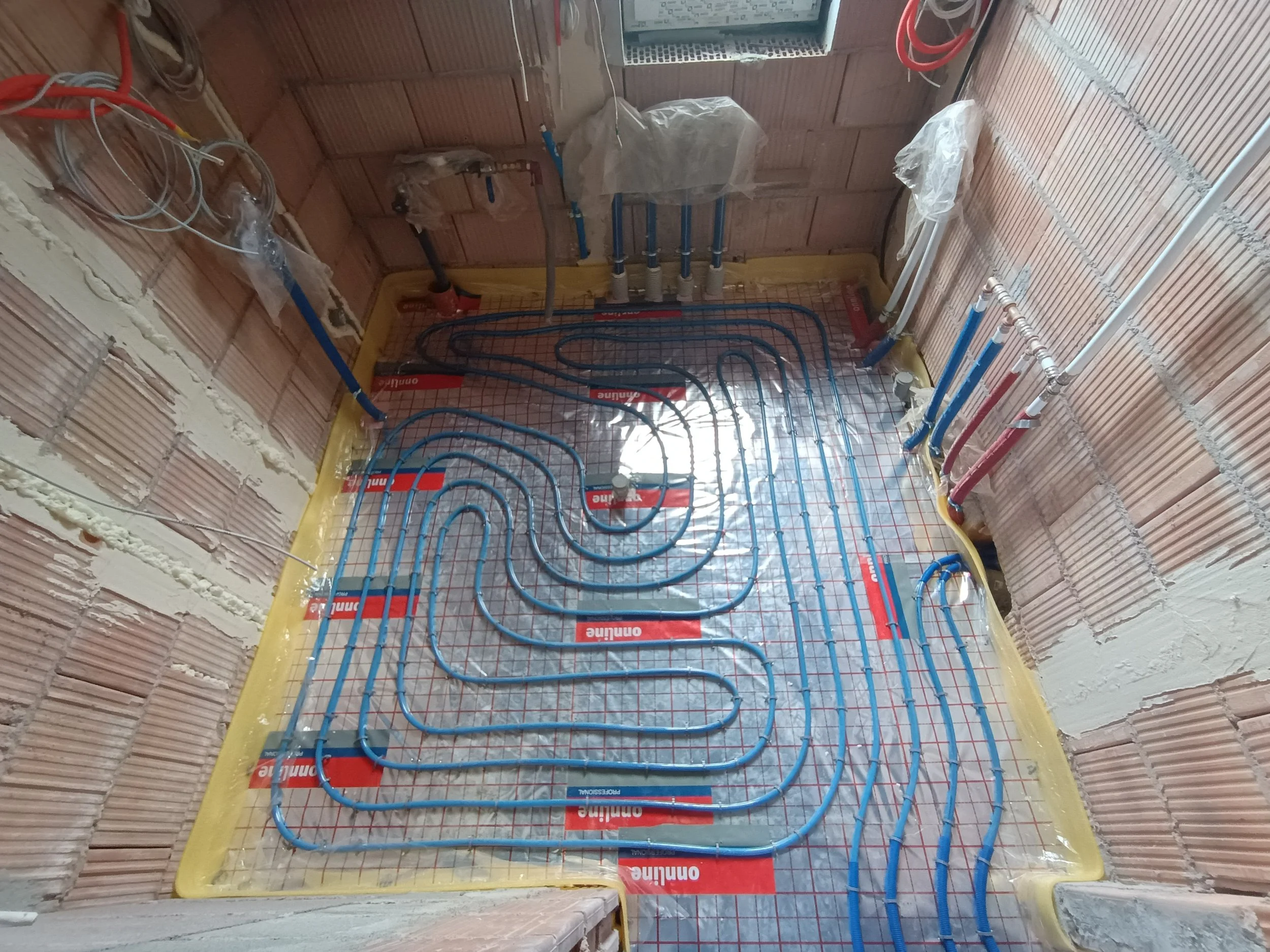Underfloor heating pipes installed in a room with brick walls and exposed plumbing.