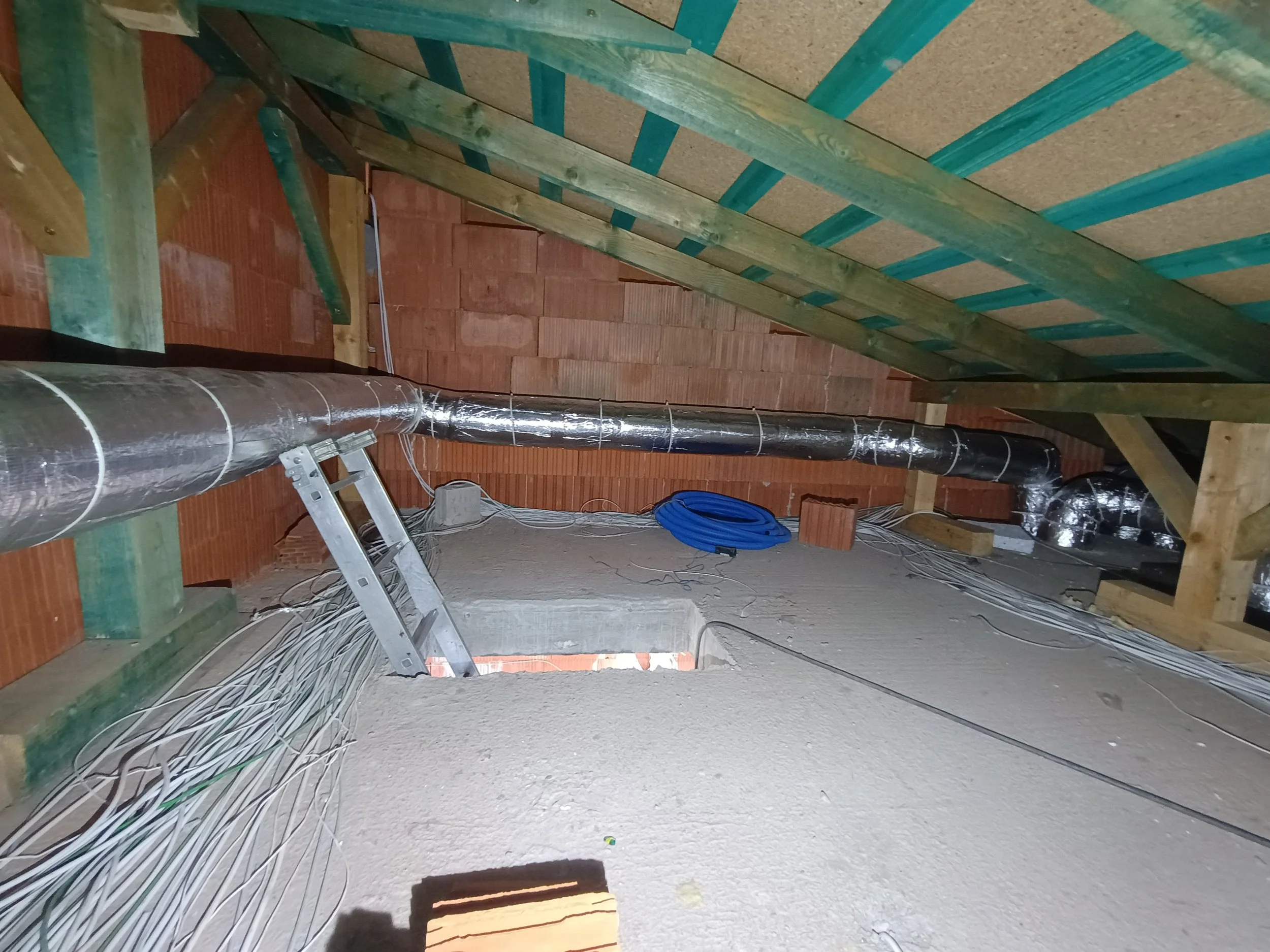 The image shows an unfinished attic space with exposed wooden framing, a metal duct running along the floor, and a clutter of electrical wires. A small ladder is leaning against the wall, and a coil of blue tubing is on the floor. The ceiling is part