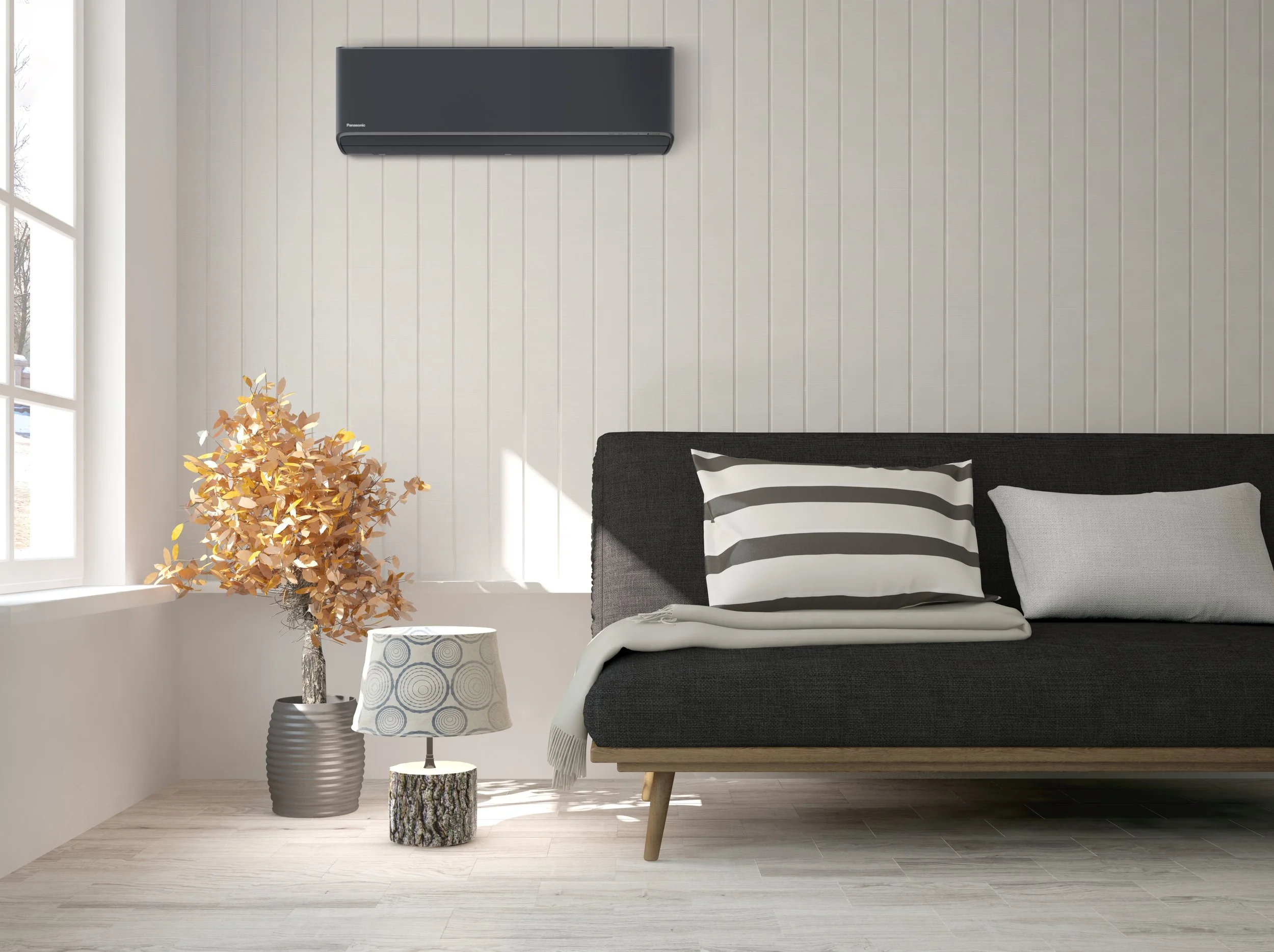 Living room corner with a dark gray sofa, a potted dried plant, a small tree stump side table, a patterned lamp, a wall-mounted air conditioner, and a window with sunlight.