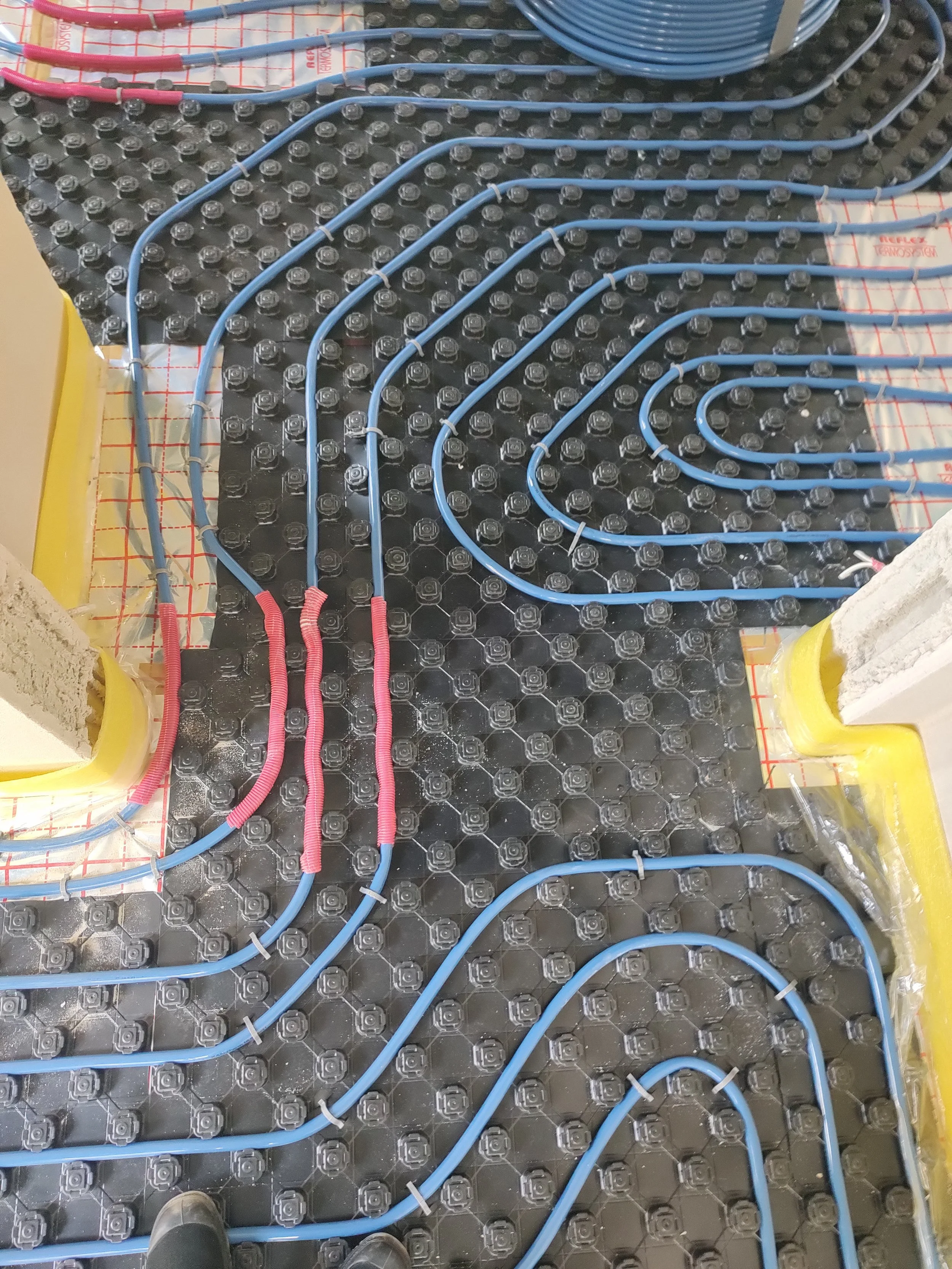 Blue electrical conductors arranged on a black surface with a grid pattern, connected to a yellow insulation box on each side, with red and blue insulated wires and white zip ties.