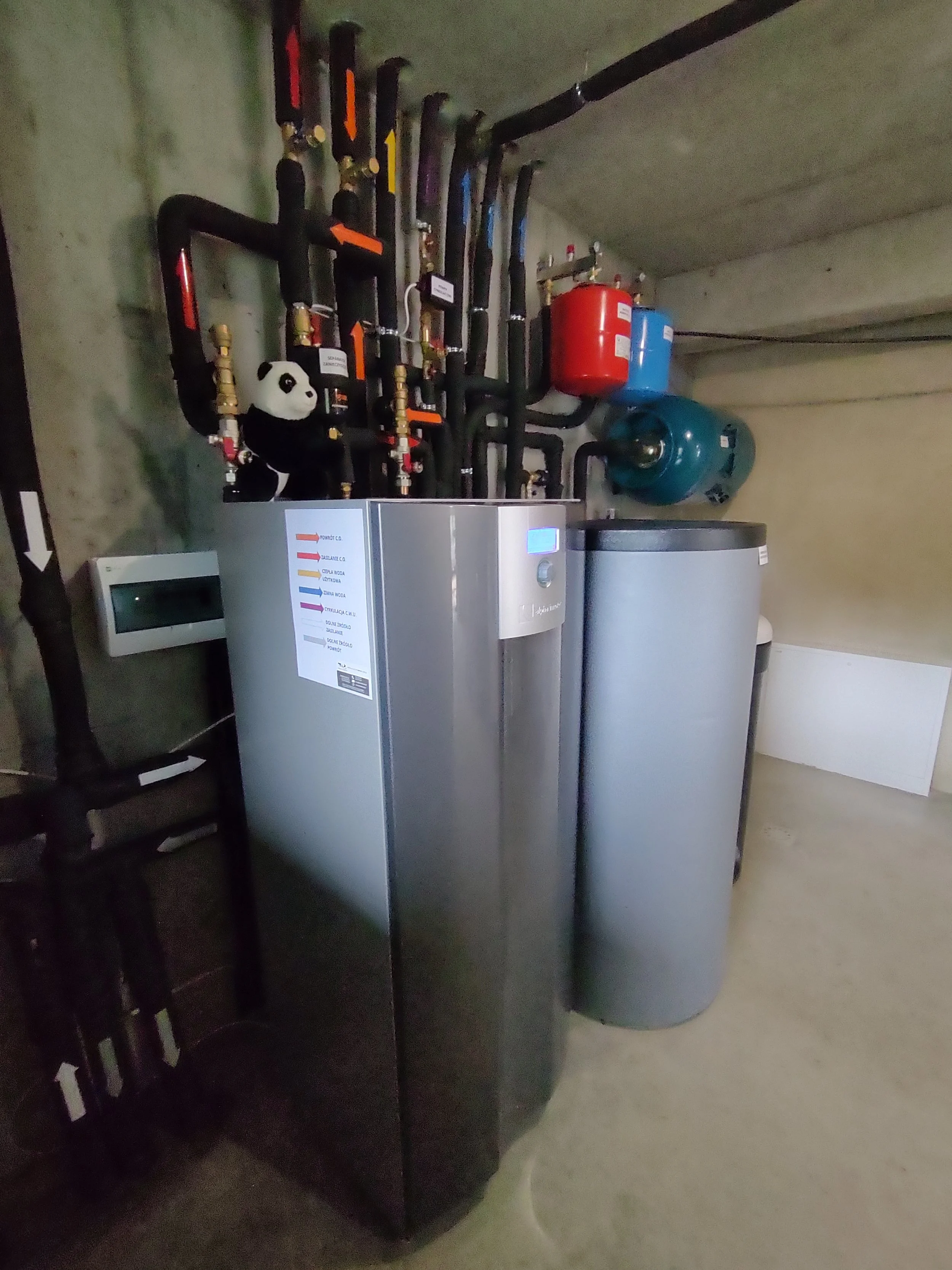 Room with pipes, a panda plush toy, and a boiler system with a control panel.