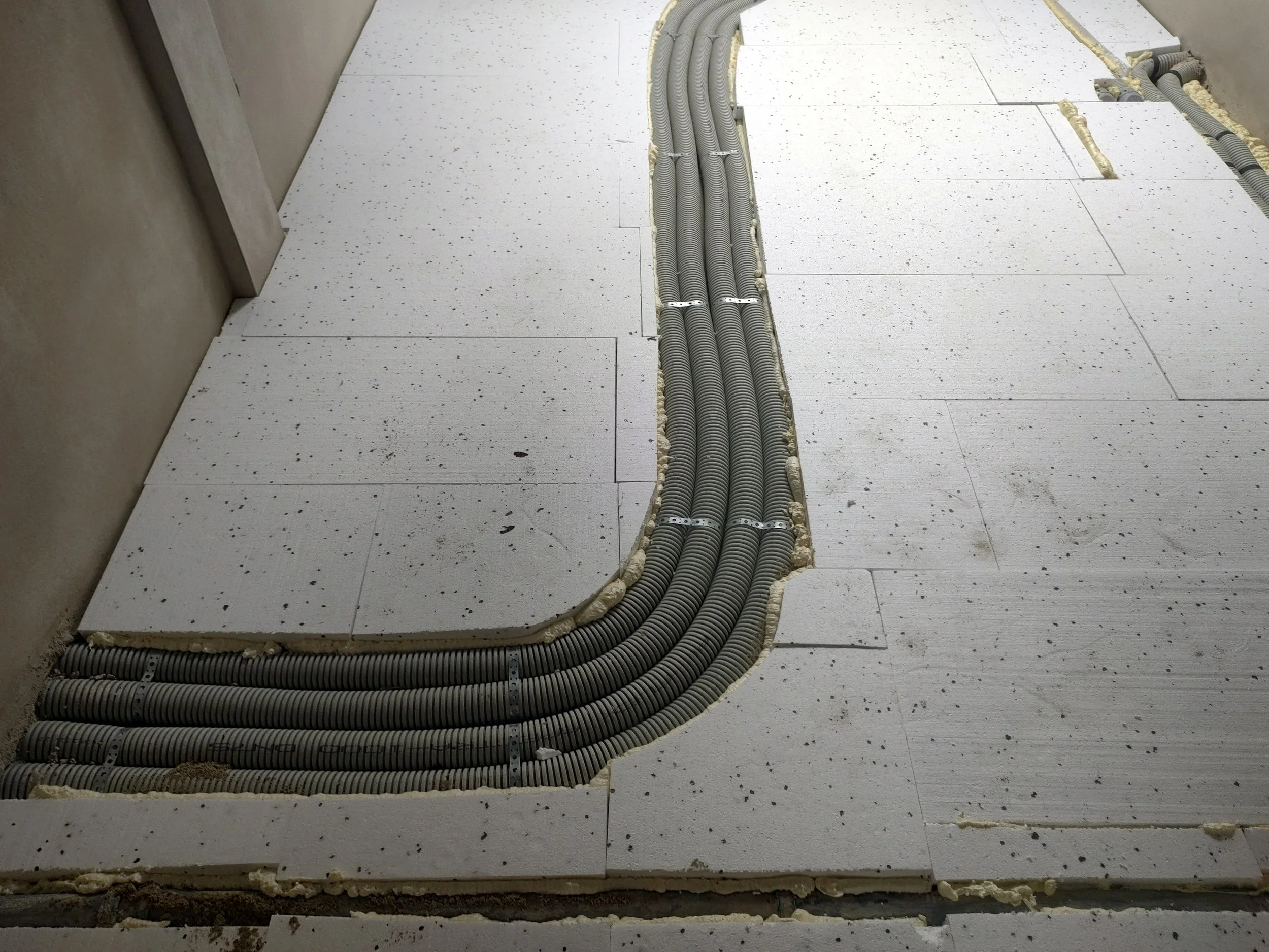 Electrical conduits installed in a building under construction, embedded in the floor showing multiple grey flexible pipes organized and secured in a trench.