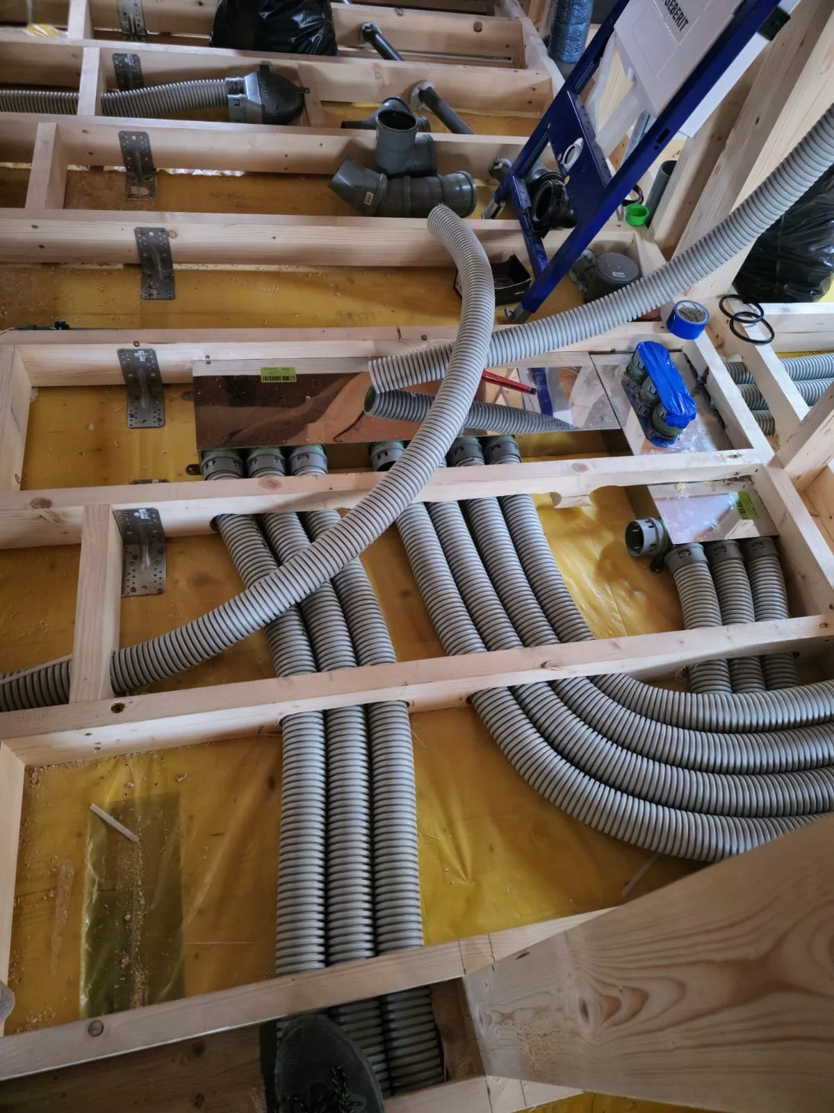 Construction site showing wooden framing with multiple electrical conduits and fittings installed.