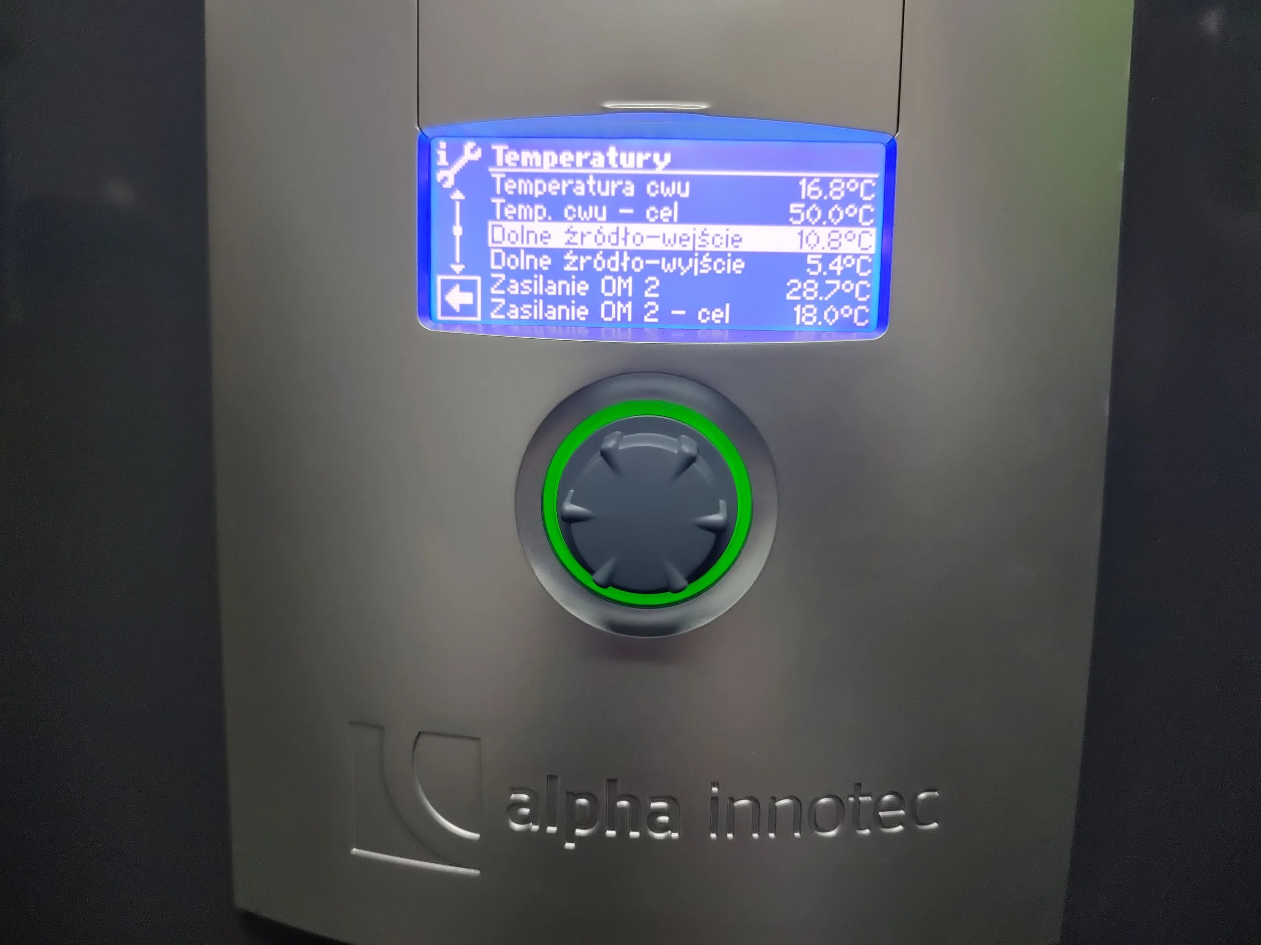 A digital display screen showing temperature readings, with a green circle around a control knob below the screen and the text 'alpha innotec' at the bottom.