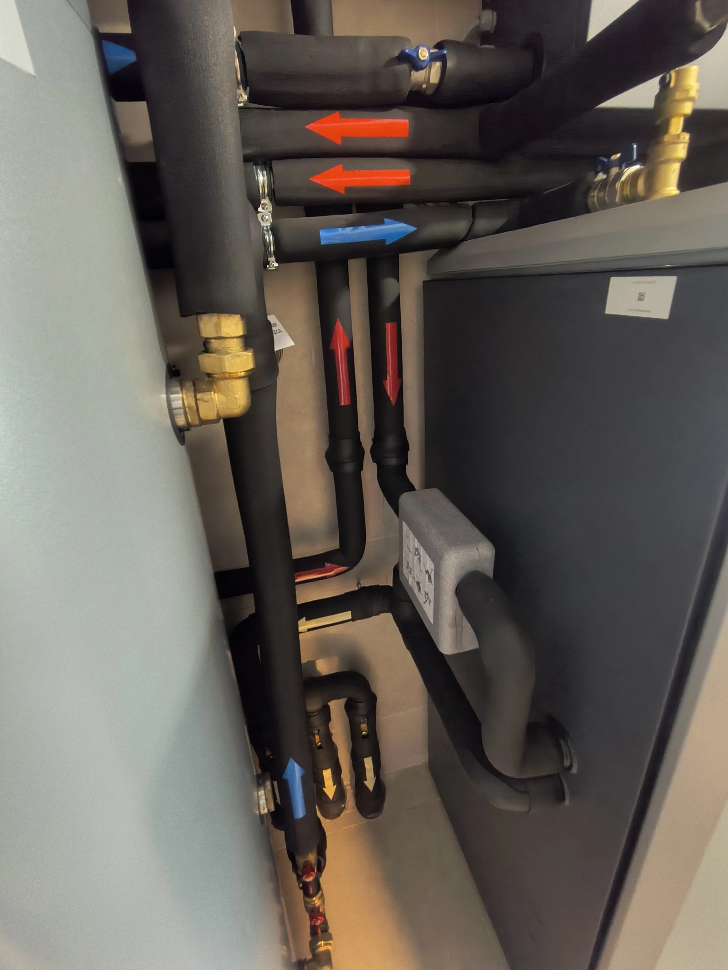 An array of black pipes with colored arrows and brass fittings in an indoor setting, likely part of a plumbing or heating system.