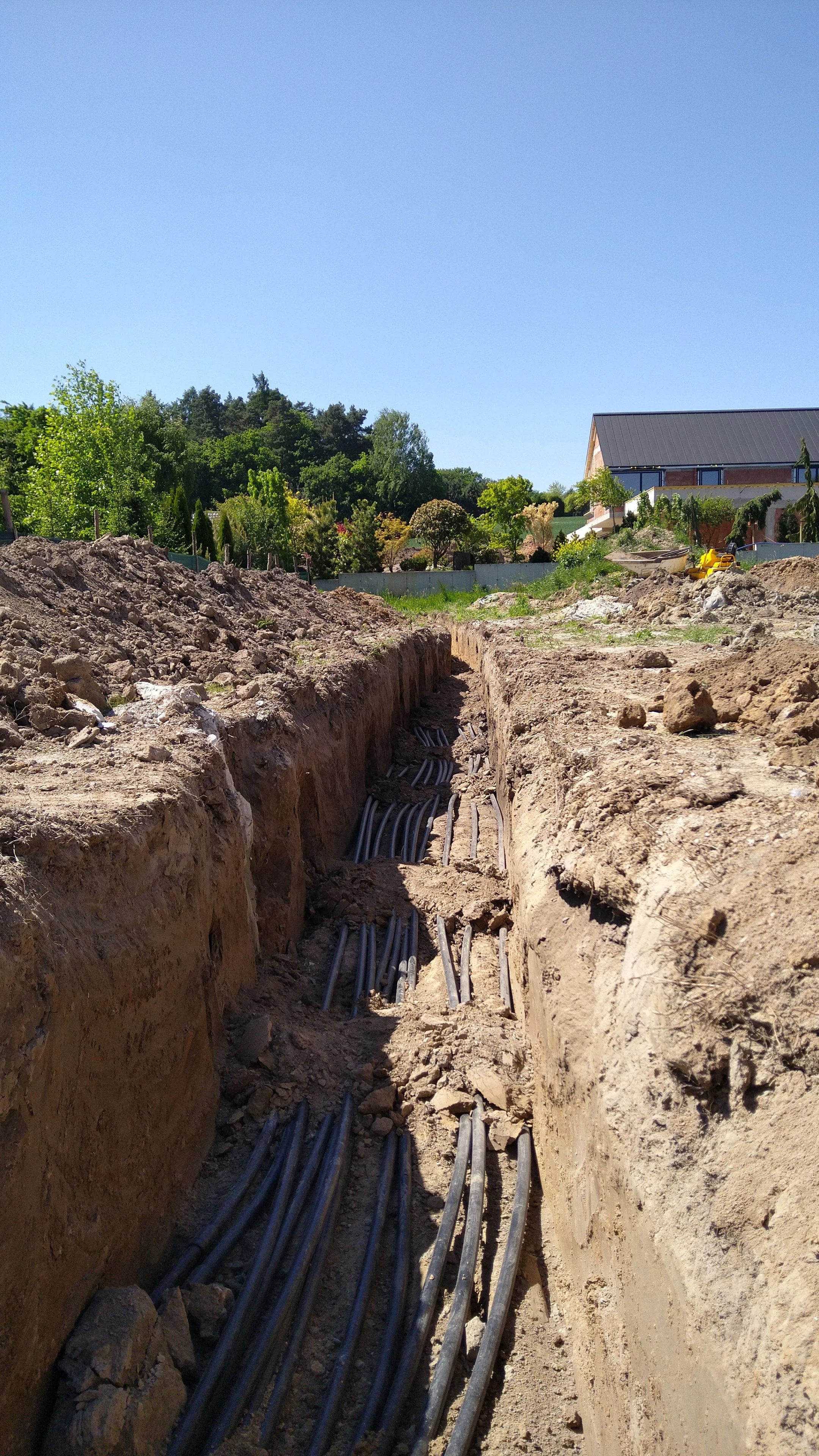 Construction site with underground utility cables being installed in a trench, with residential houses and greenery visible in the background.