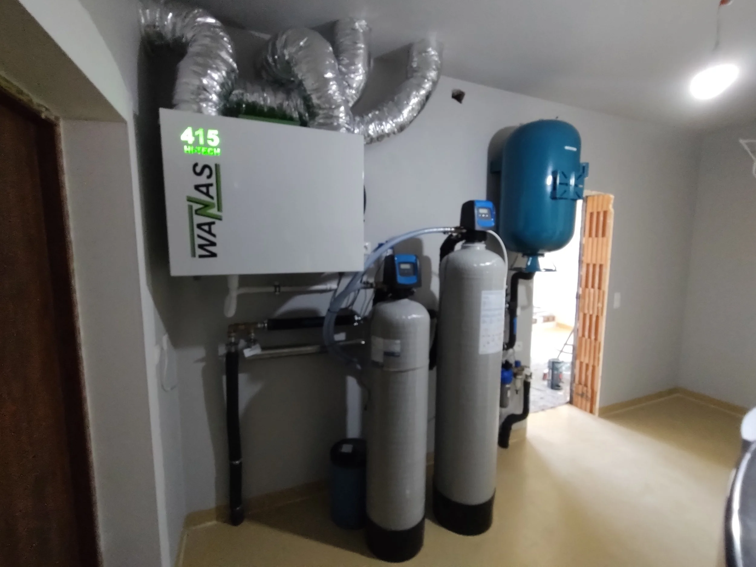 Water softening or filtration system with tanks, gauges, and a blue air tank in a utility closet.