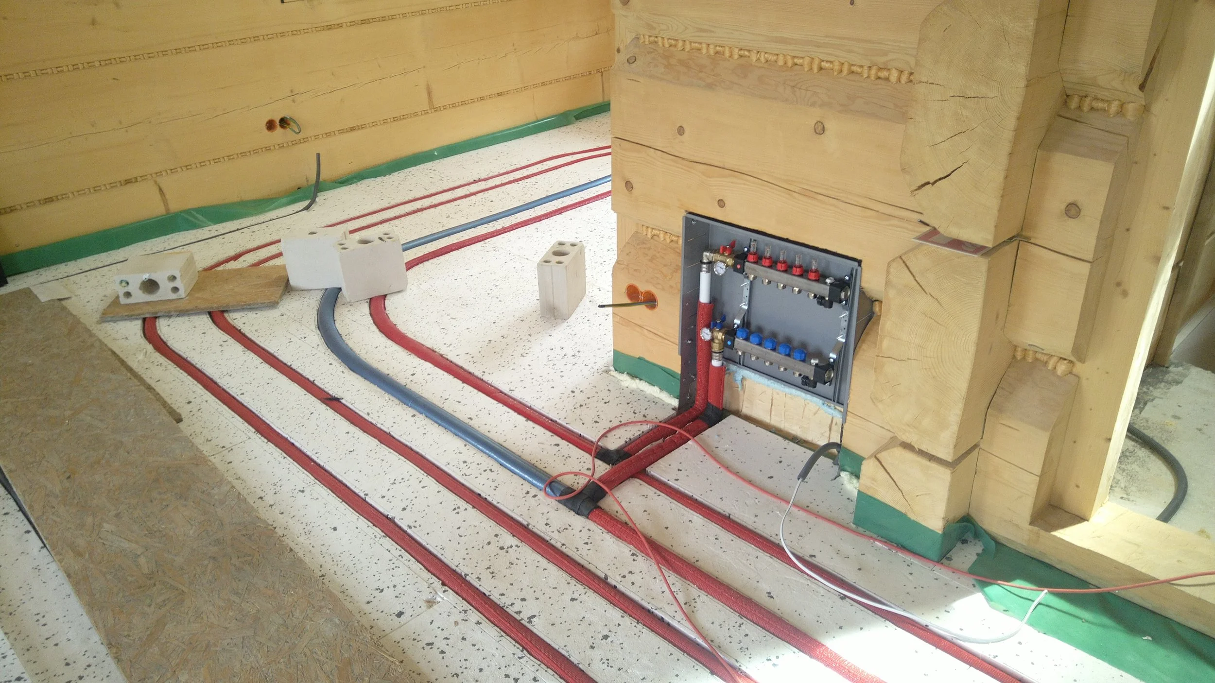 Construction site showing electrical wiring, pipes, and insulation within a wooden wall during construction.