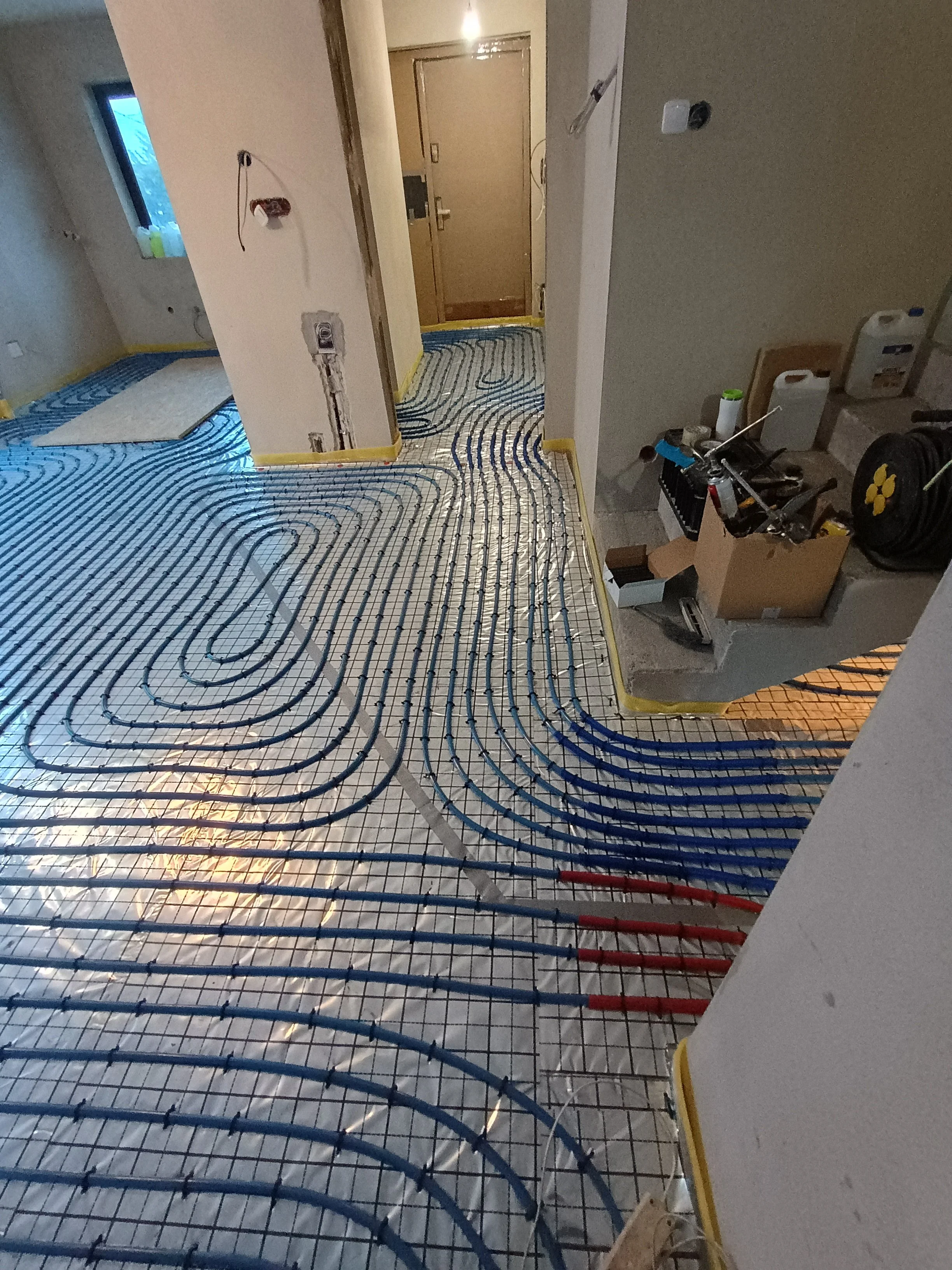 Loft or apartment under construction with heated floor tubing visible on the floor surface and some construction tools and materials on the right side.
