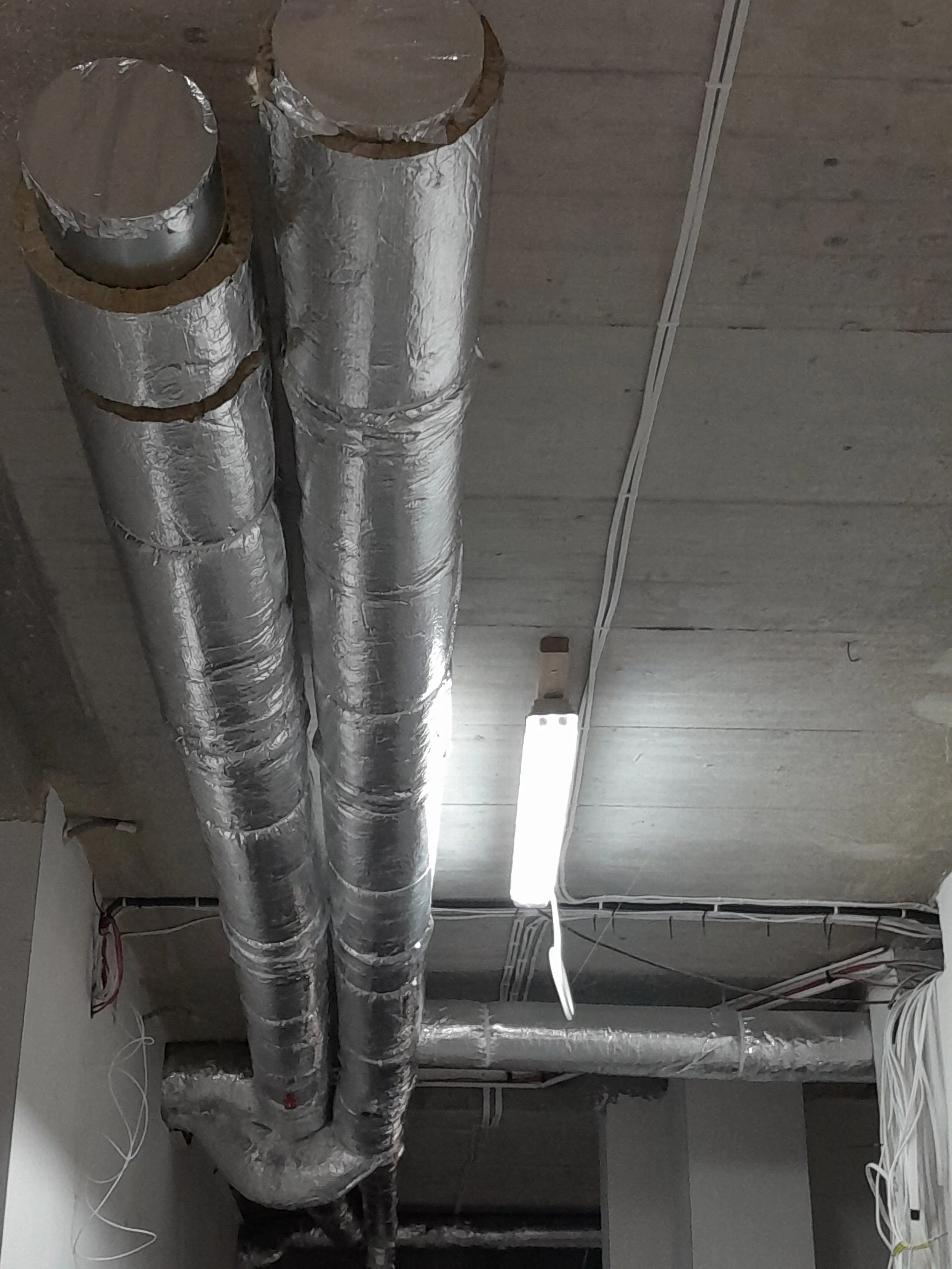 Ceiling with silver insulated ductwork and electrical wiring, fluorescent light fixture, and ceiling grid with some visible wires.