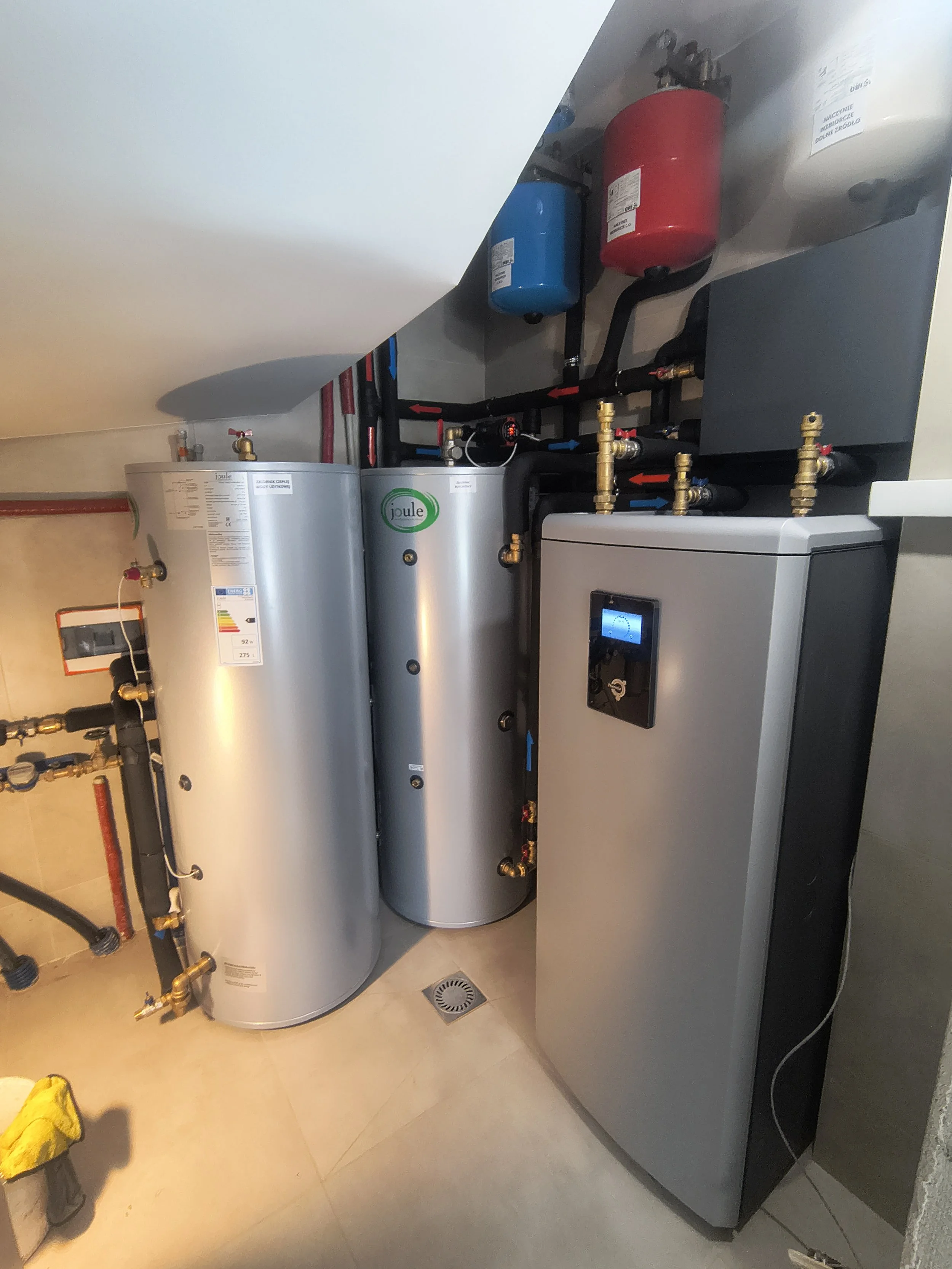 A water heater, a boiler with an electronic control panel, and two large red and blue expansion tanks mounted above the boiler, all installed in a utility room.