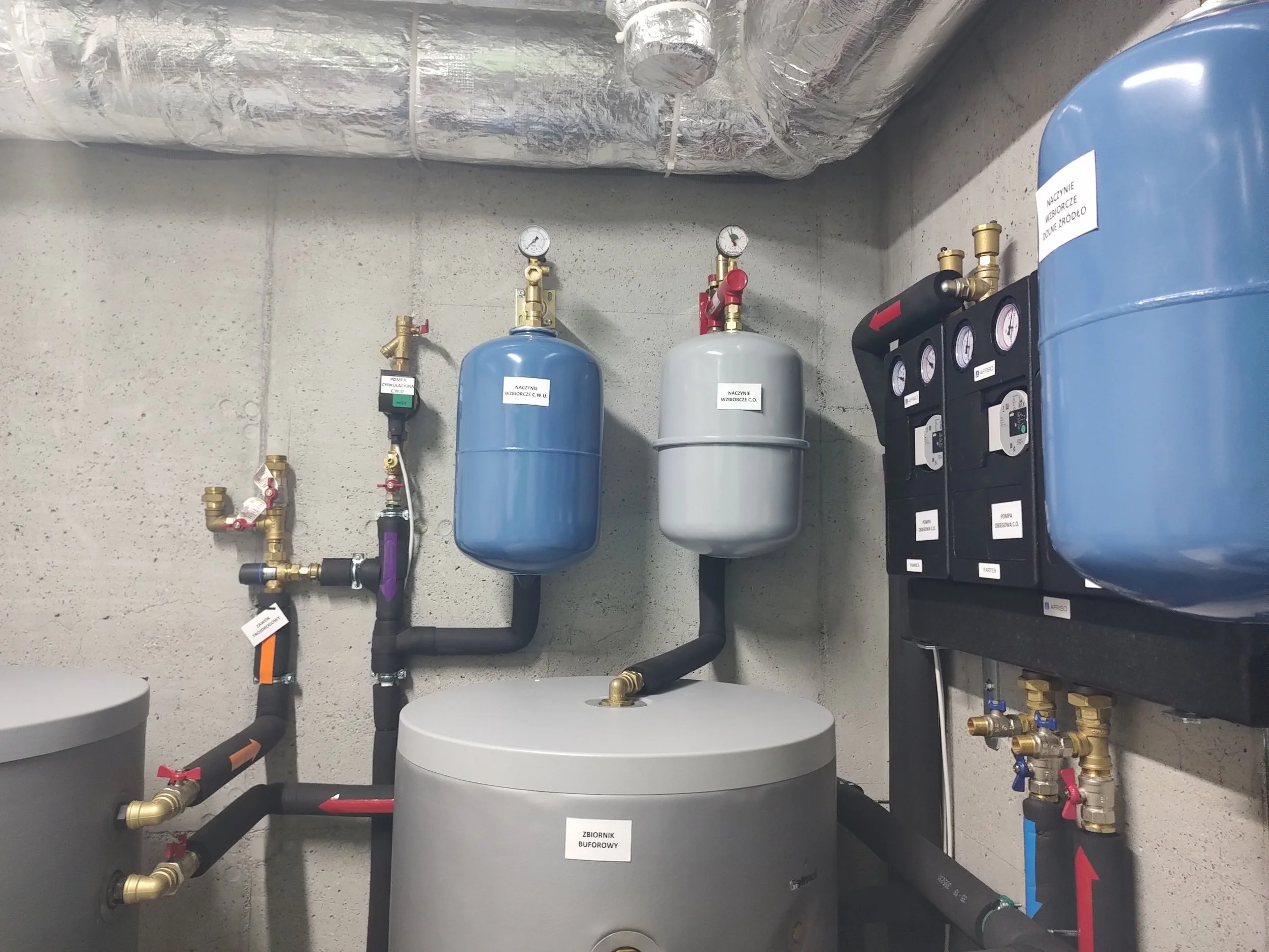 Mechanical room with tanks, gauges, pipes, and control panels.