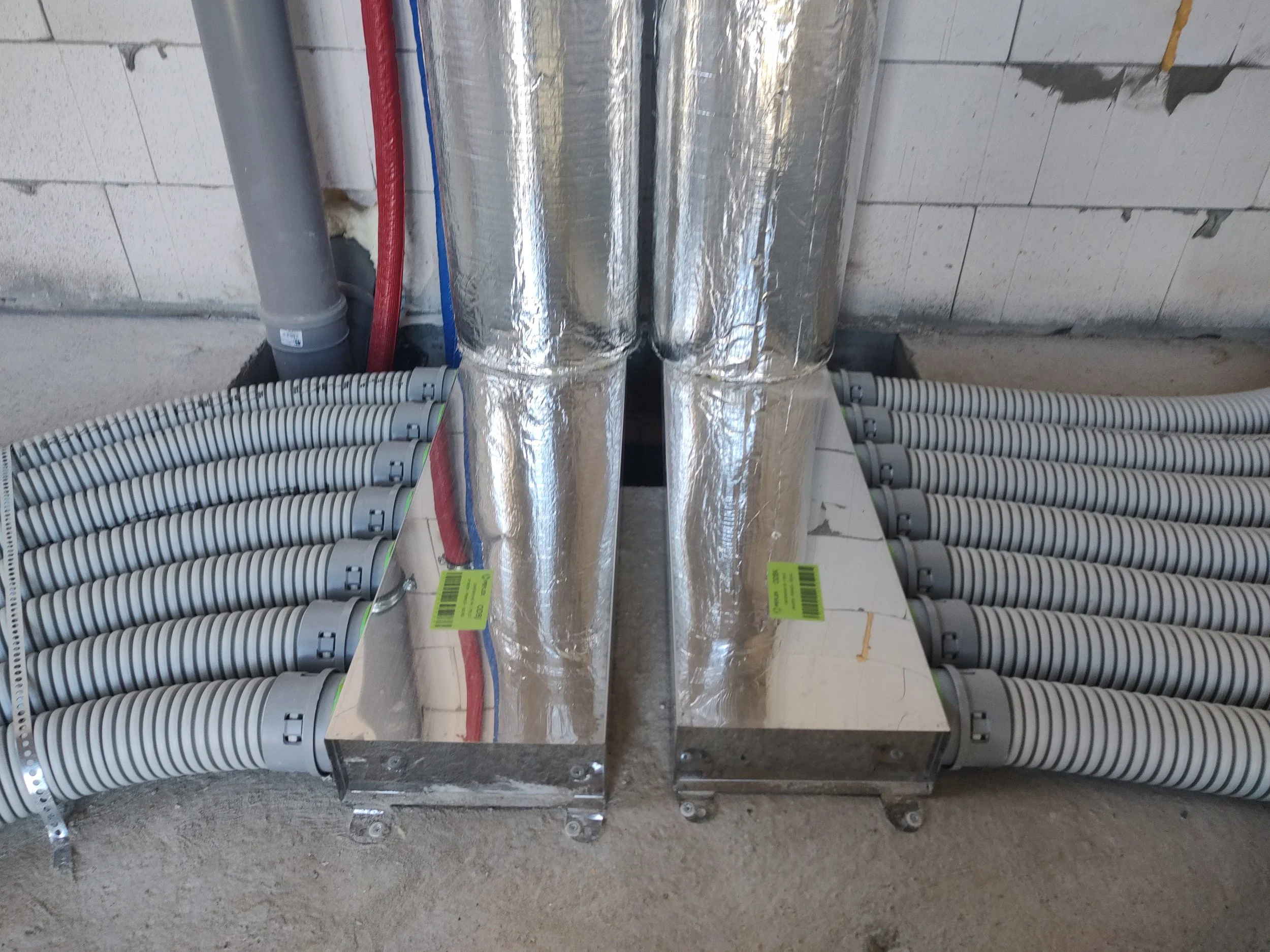 Installation of HVAC ductwork with insulated aluminum ducts, plastic electrical conduit pipes, and concrete block wall in a building construction site.