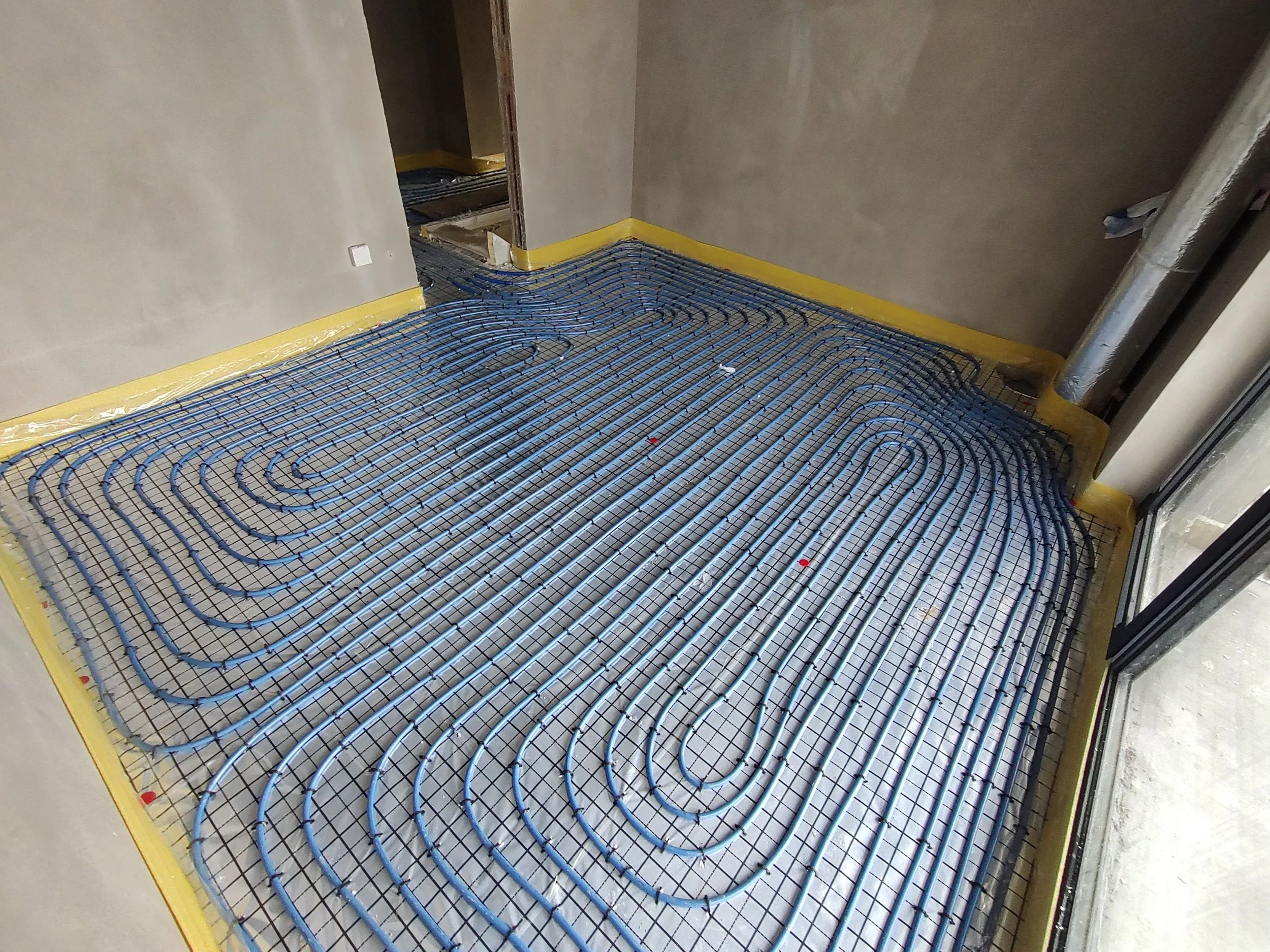 Underfloor heating pipes installed on a yellow edging in a room under construction.