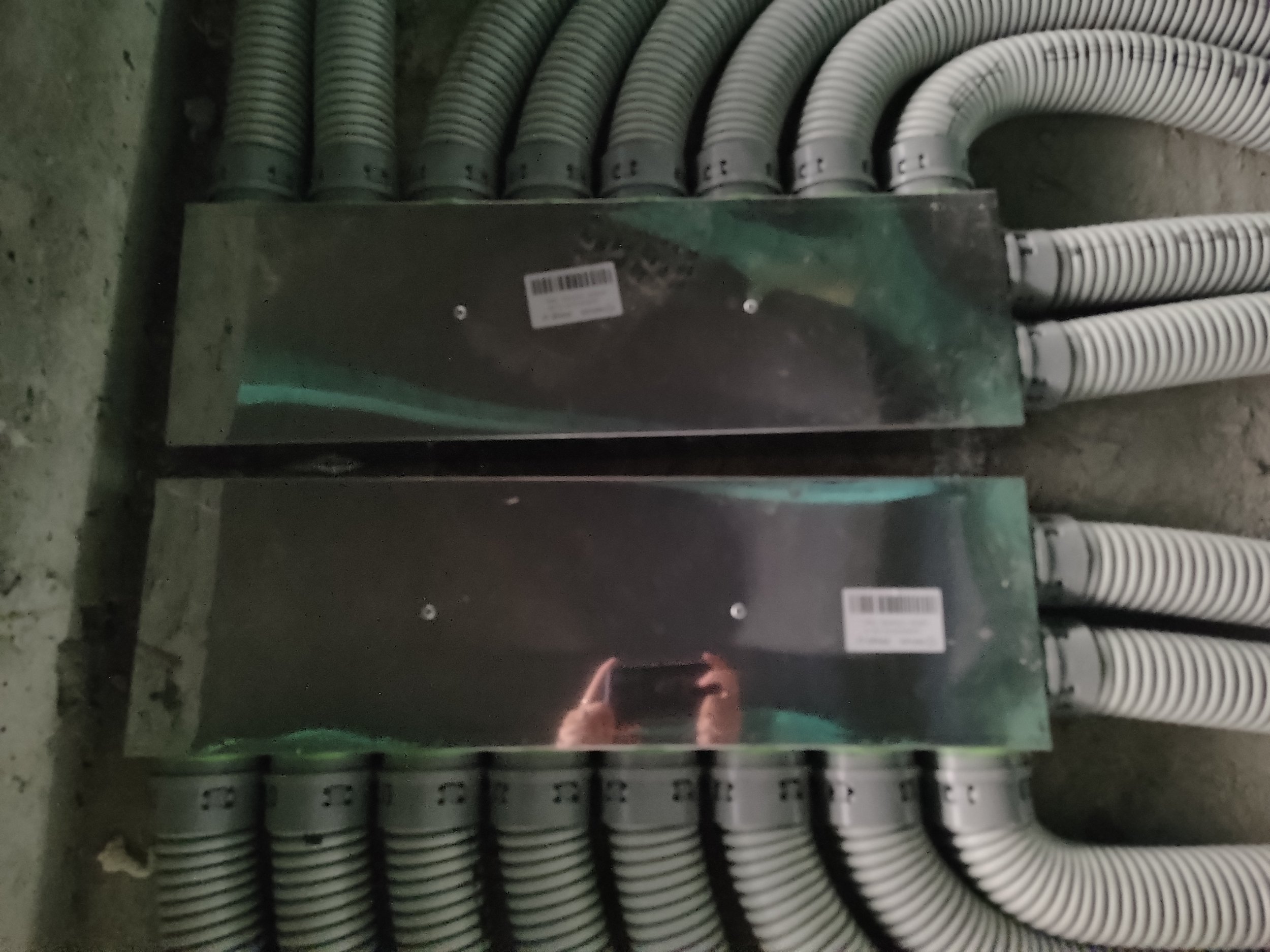 Electrical cables organized in a metal panel with a reflective surface, mounted on a concrete wall.
